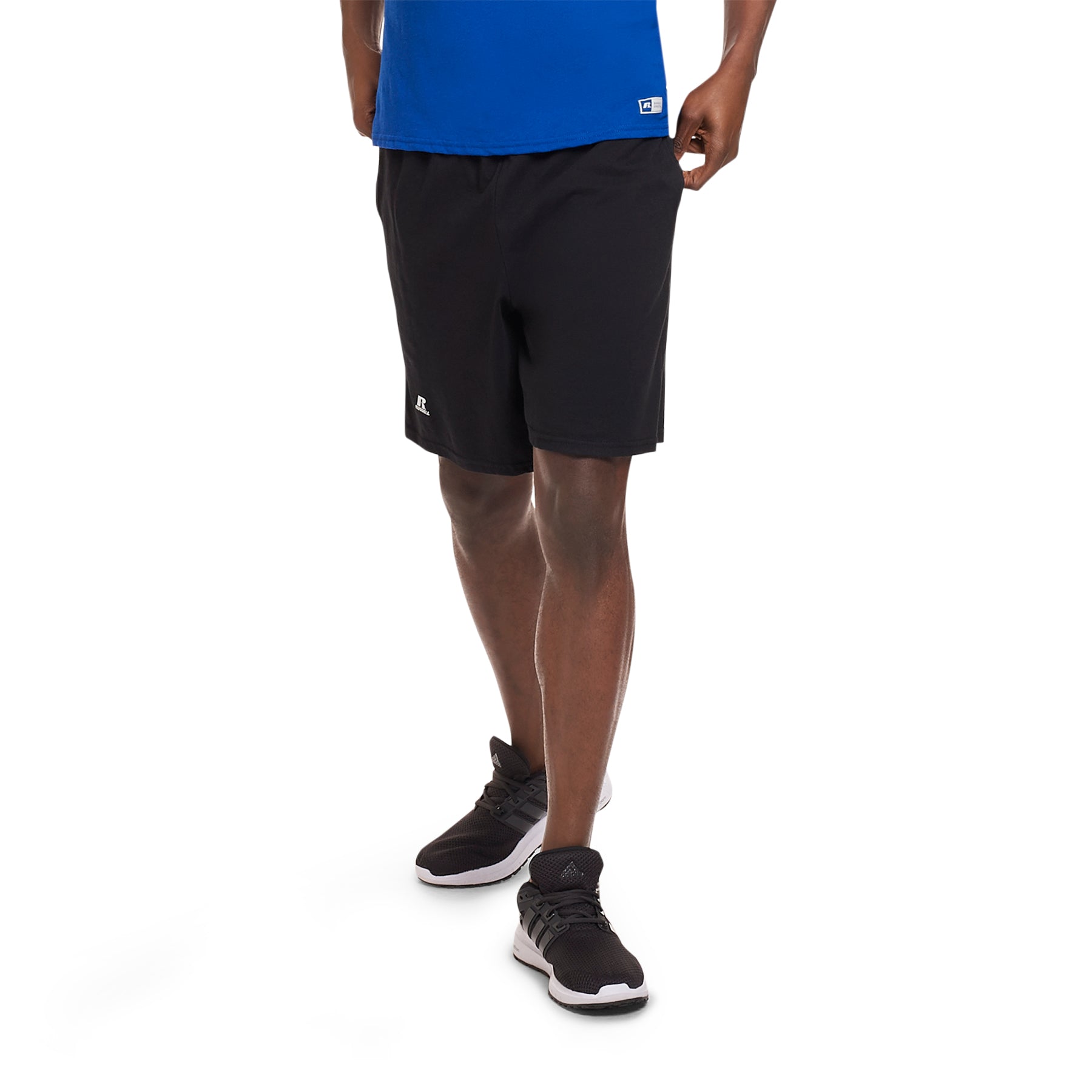 A man wearing Russell Athletic black cotton jersey pocketed sweatshorts and athletic sneakers.