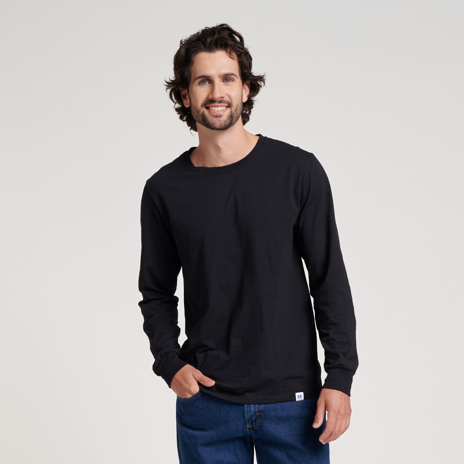 A man wearing a black Russell Athletic DRI-POWER CVC Performance unisex long-sleeve t-shirt with blue jeans.
