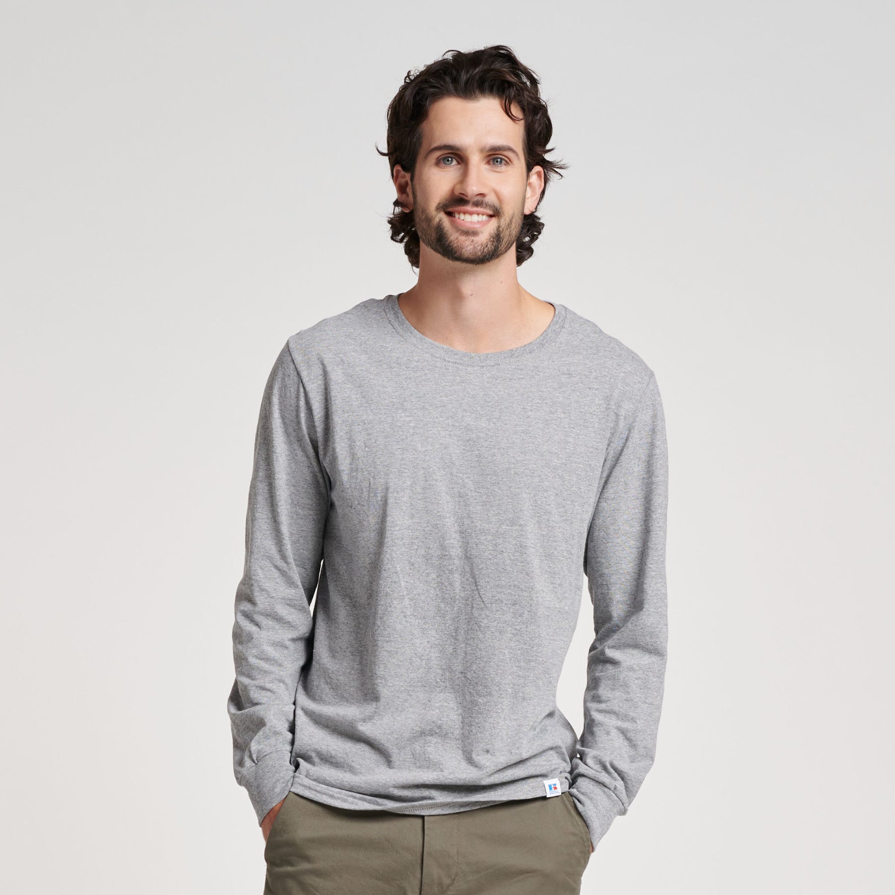 Model smiling in a Russell Athletic DRI-POWER CVC Performance Unisex Long-Sleeve T-Shirt in Oxford gray.