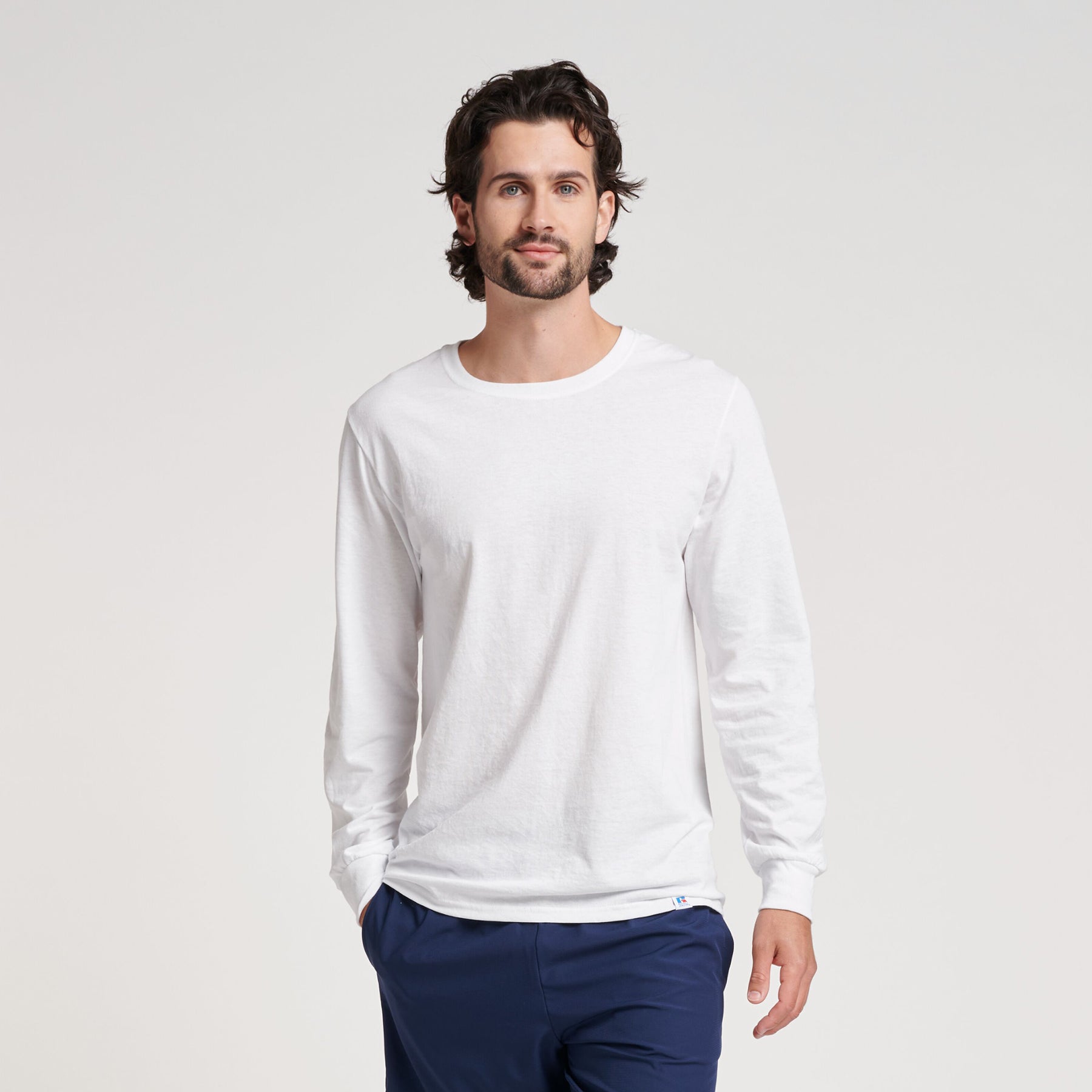 A man wearing a white Russell Athletic DRI-POWER CVC Performance Unisex Long-Sleeve T-Shirt with blue pants.