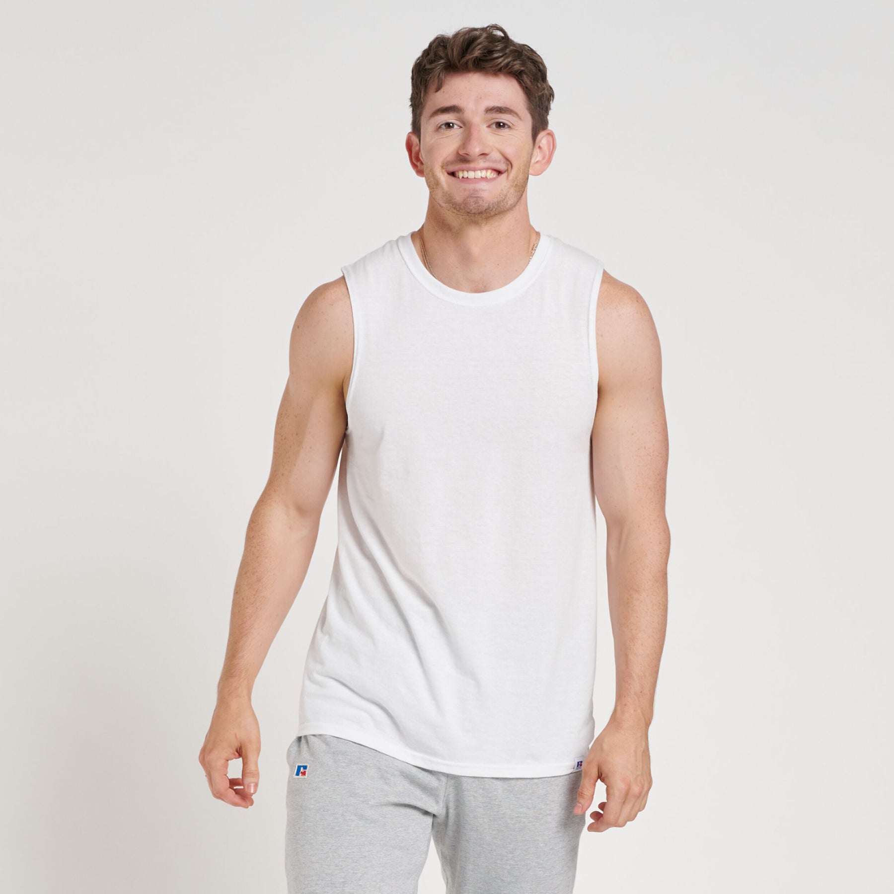 A man wearing a white Russell Athletic DRI-POWER CVC Performance unisex muscle T-shirt with grey sweatpants.