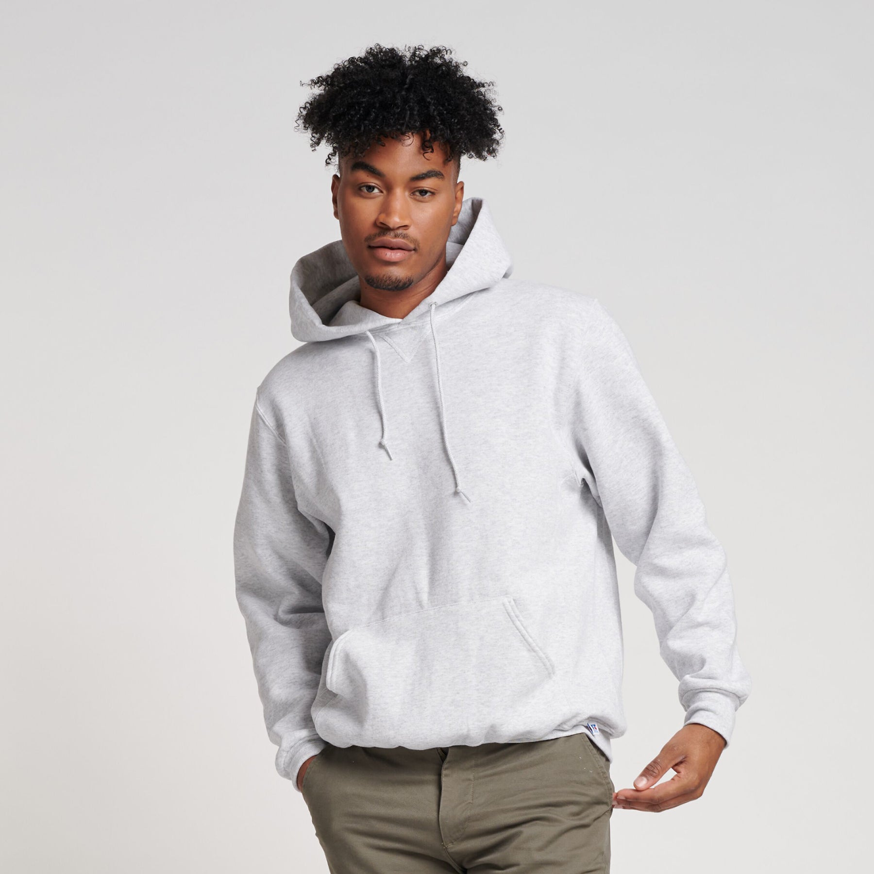 A man wearing a light ash Russell Athletic DRI-POWER Adult Fleece Unisex Hoodie in a studio setting.