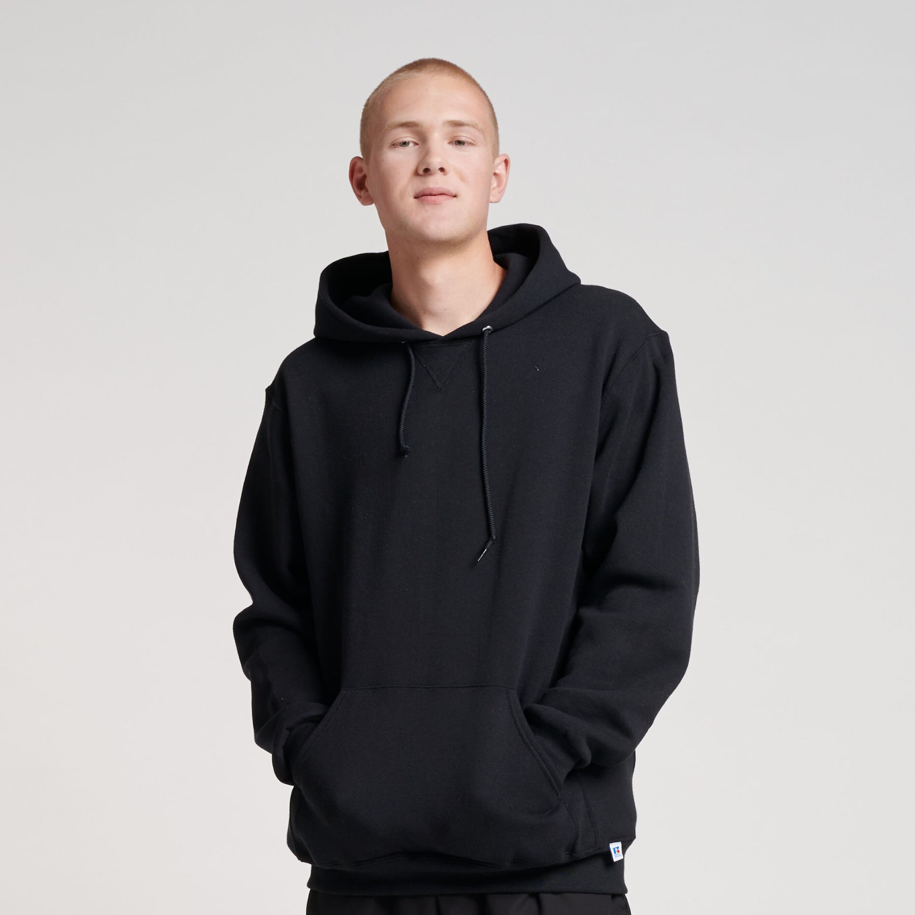 Young man wearing a black Russell Athletic DRI-POWER Adult Fleece Unisex Hoodie with hands in the front pocket.