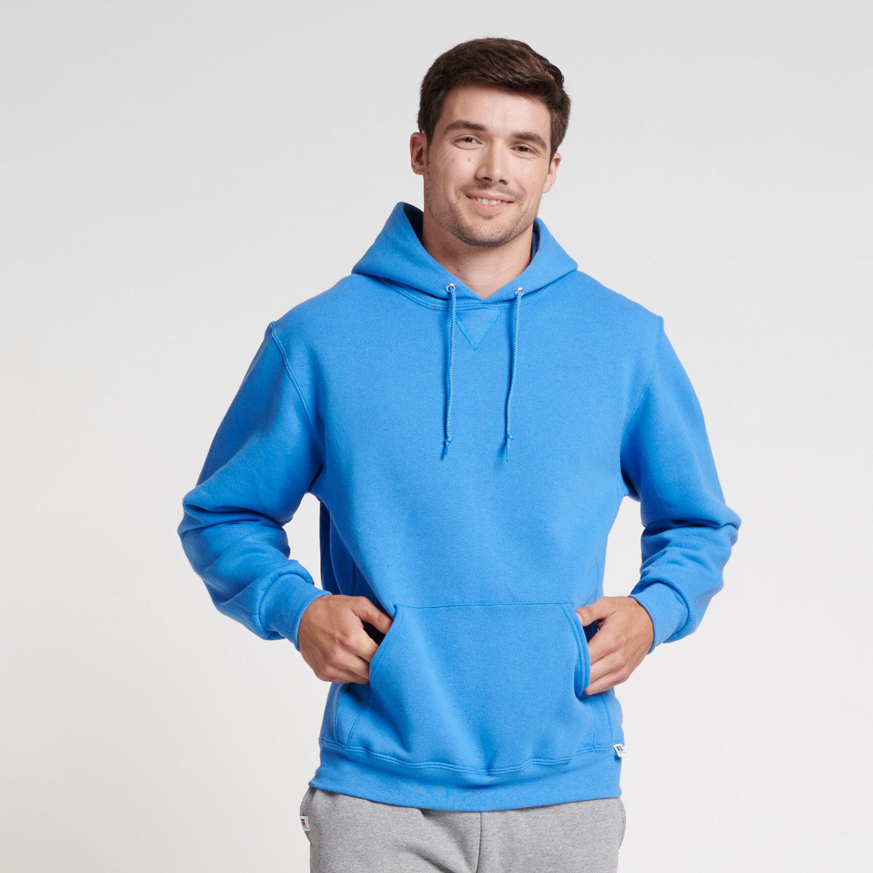 A man wearing a Russell Athletic DRI-POWER Adult Fleece Unisex Hoodie in Collegiate Blue with his hands in the pocket.