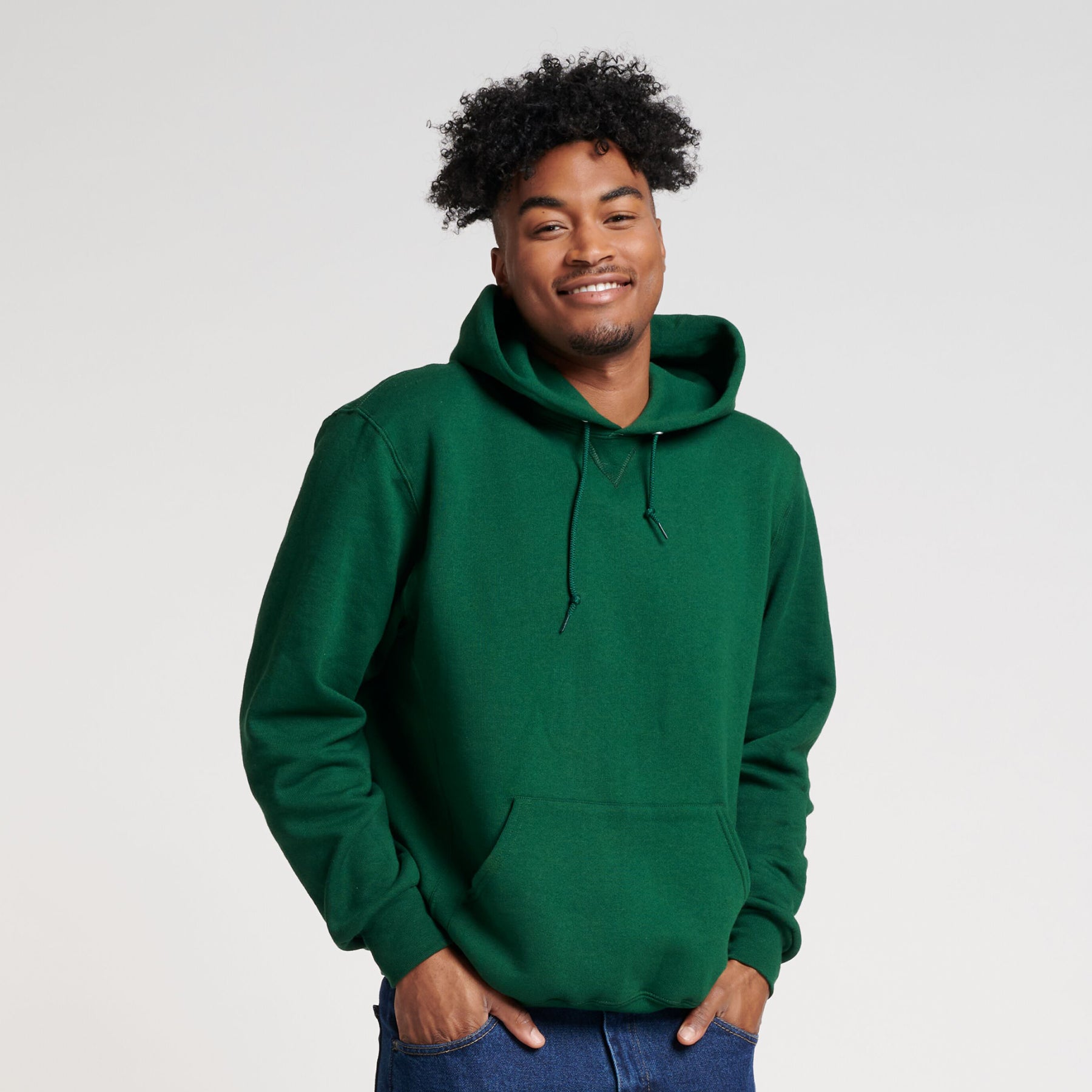 A smiling man wears a dark green Russell Athletic DRI-POWER® Adult Fleece Unisex Hoodie against a white background.