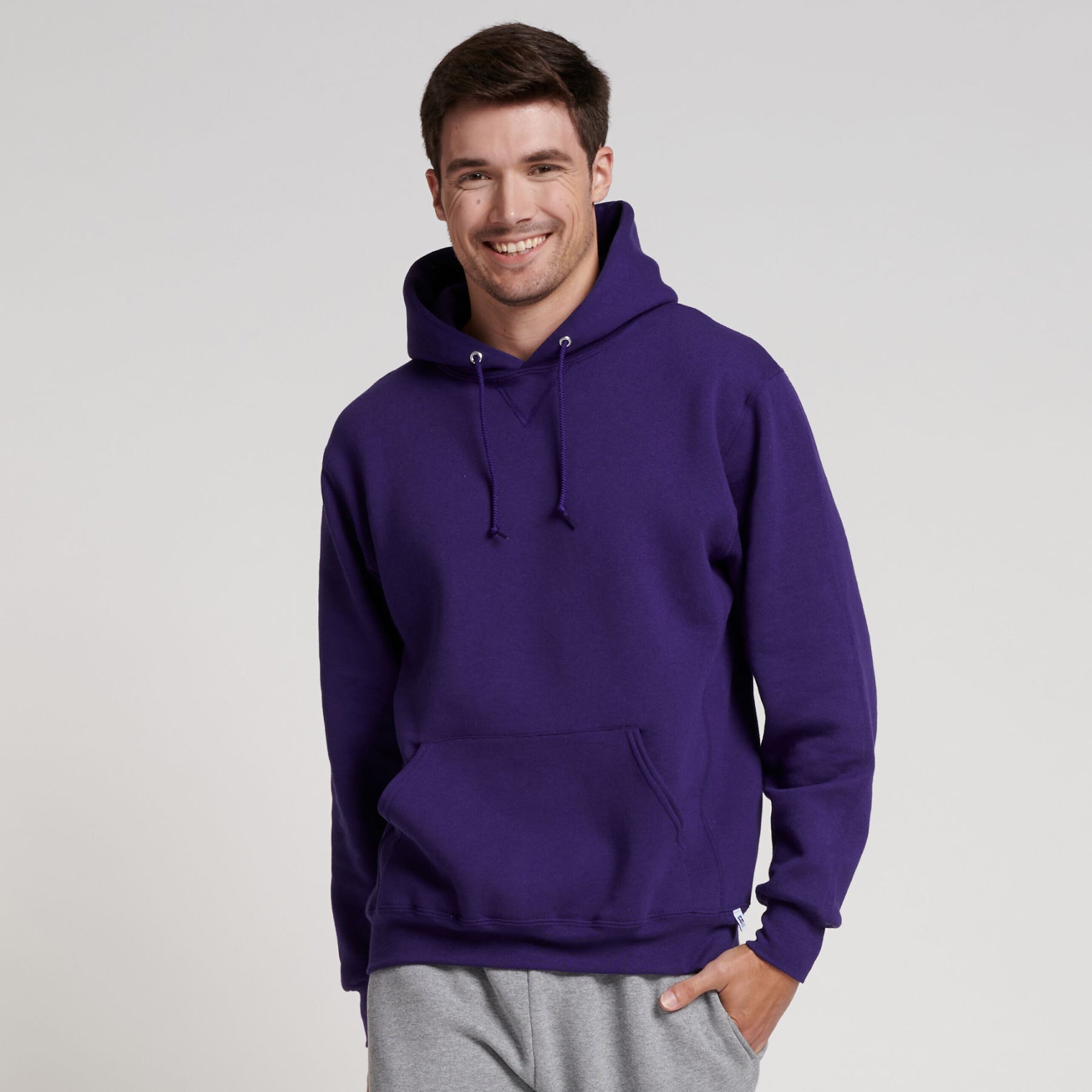 A smiling man wearing a purple Russell Athletic DRI-POWER Adult Fleece Unisex Hoodie paired with gray sweatpants.