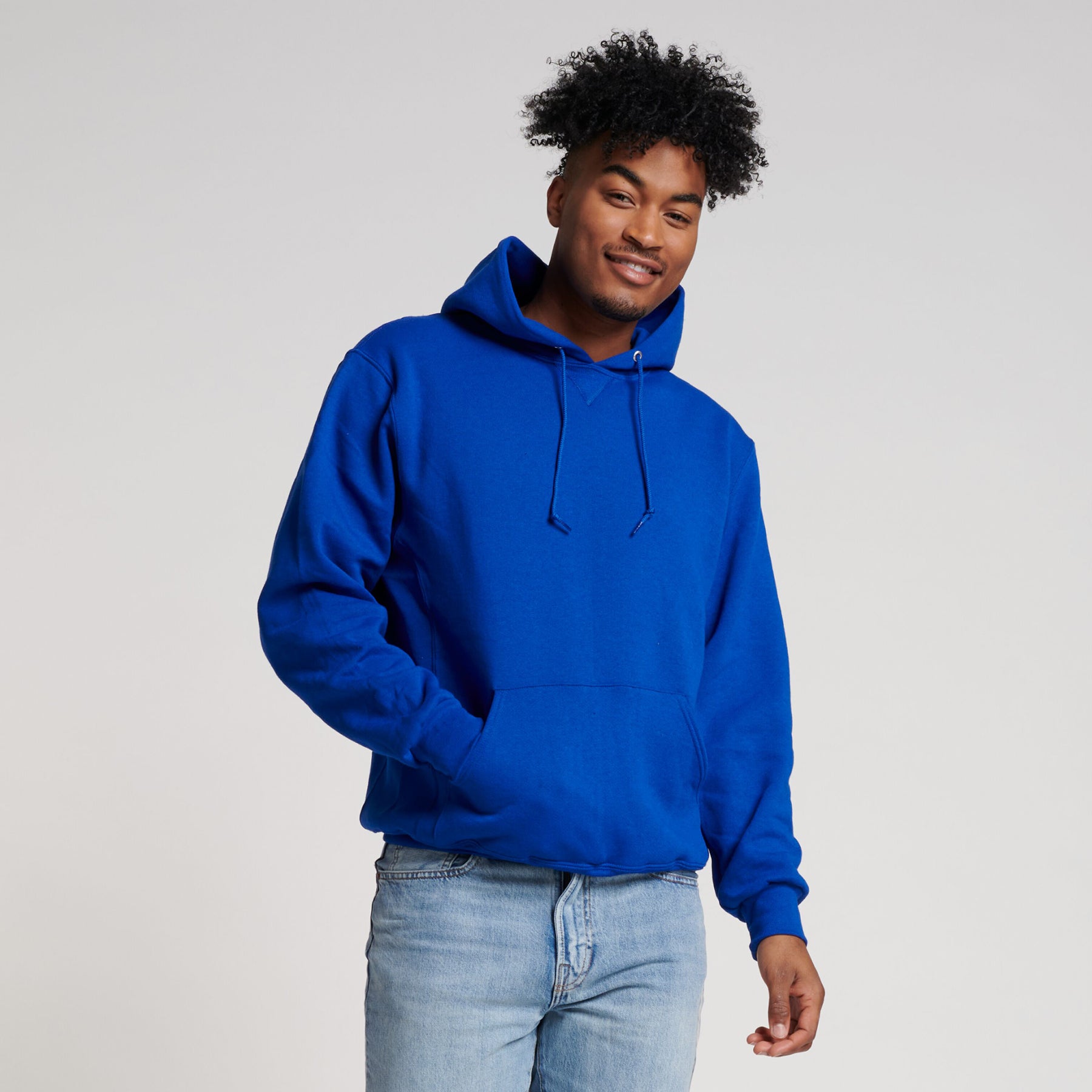 A man with curly hair wearing a royal blue Russell Athletic DRI-POWER Adult Fleece Unisex Hoodie and light blue jeans.