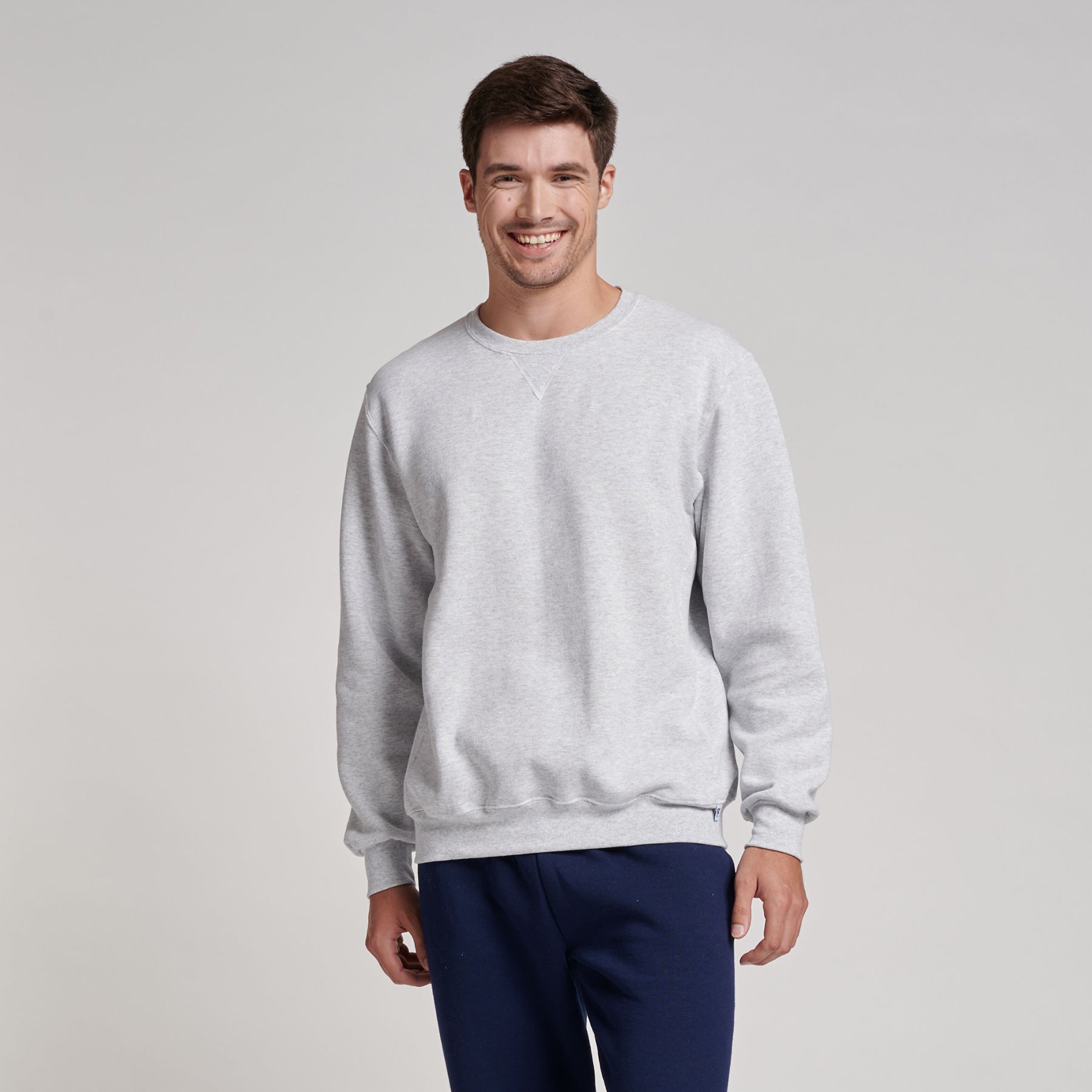 A smiling model wears a gray Russell Athletic DRI-POWER Adult Fleece Crew sweatshirt against a light background.