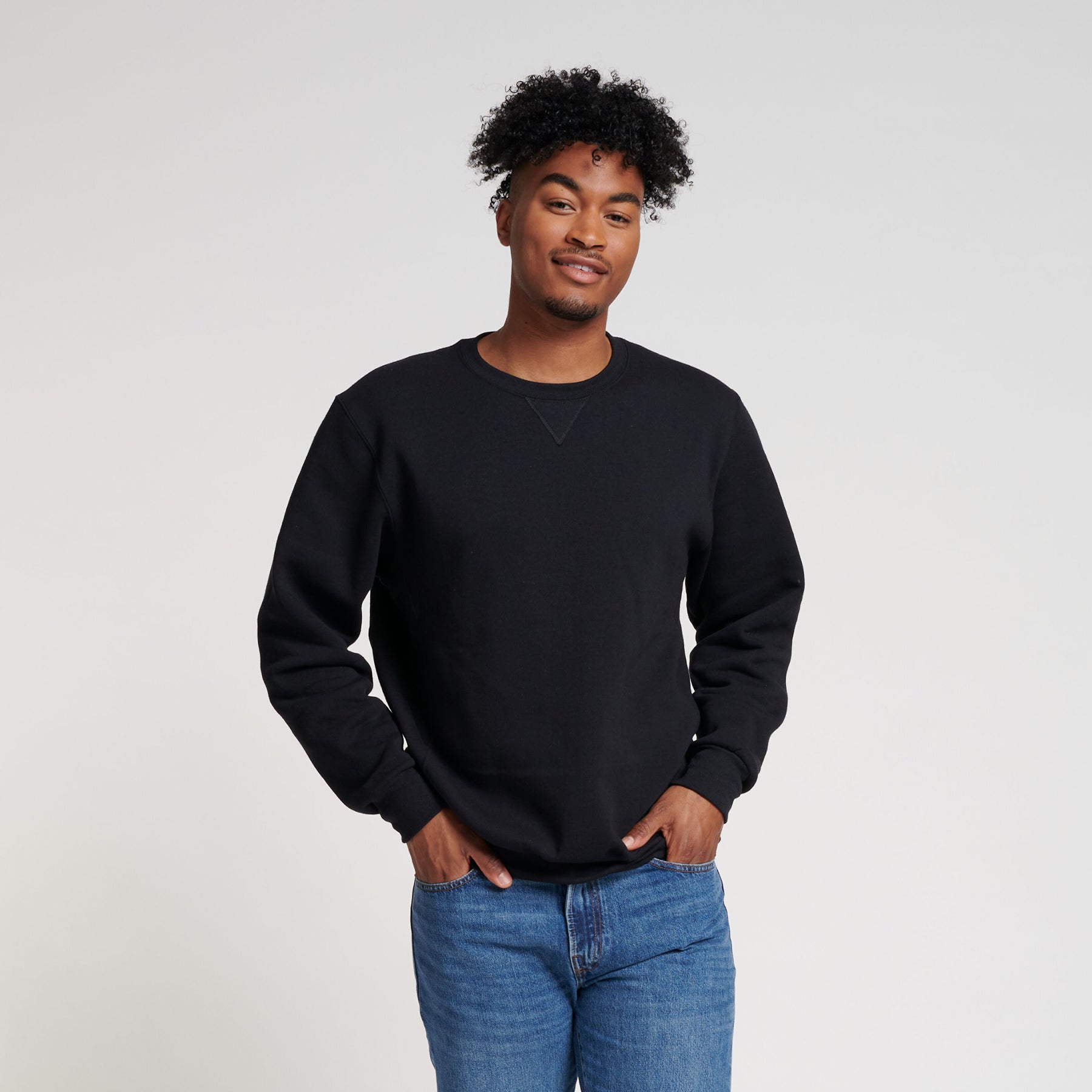 A man with curly hair wearing a black Russell Athletic DRI-POWER Adult Fleece Crew sweatshirt and blue jeans.