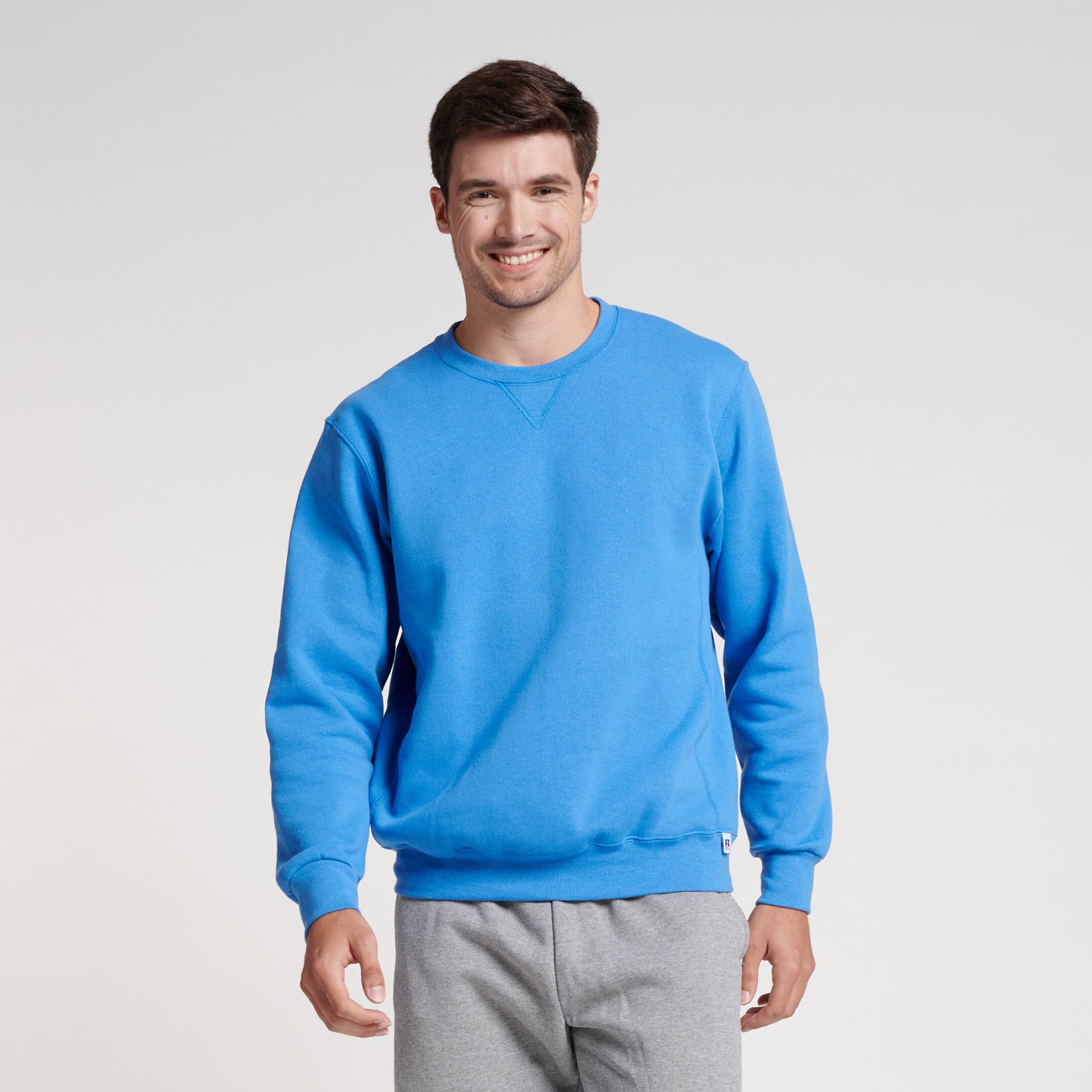 Russell Athletic DRI-POWER Adult Fleece Crew sweatshirt in Collegiate Blue worn by a smiling man against a white background.