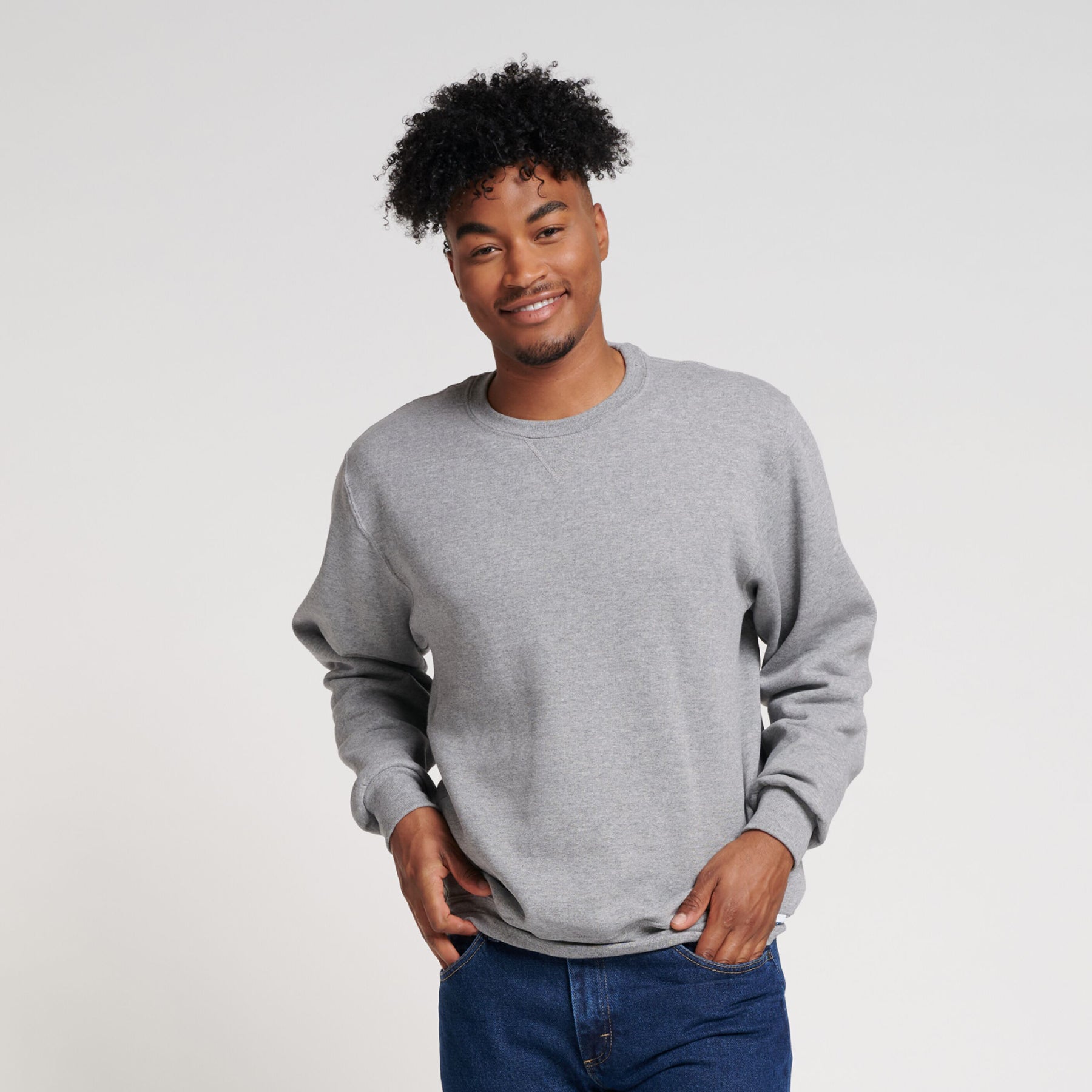 A smiling model wearing an Oxford grey Russell Athletic DRI-POWER Adult Fleece Crew sweatshirt.
