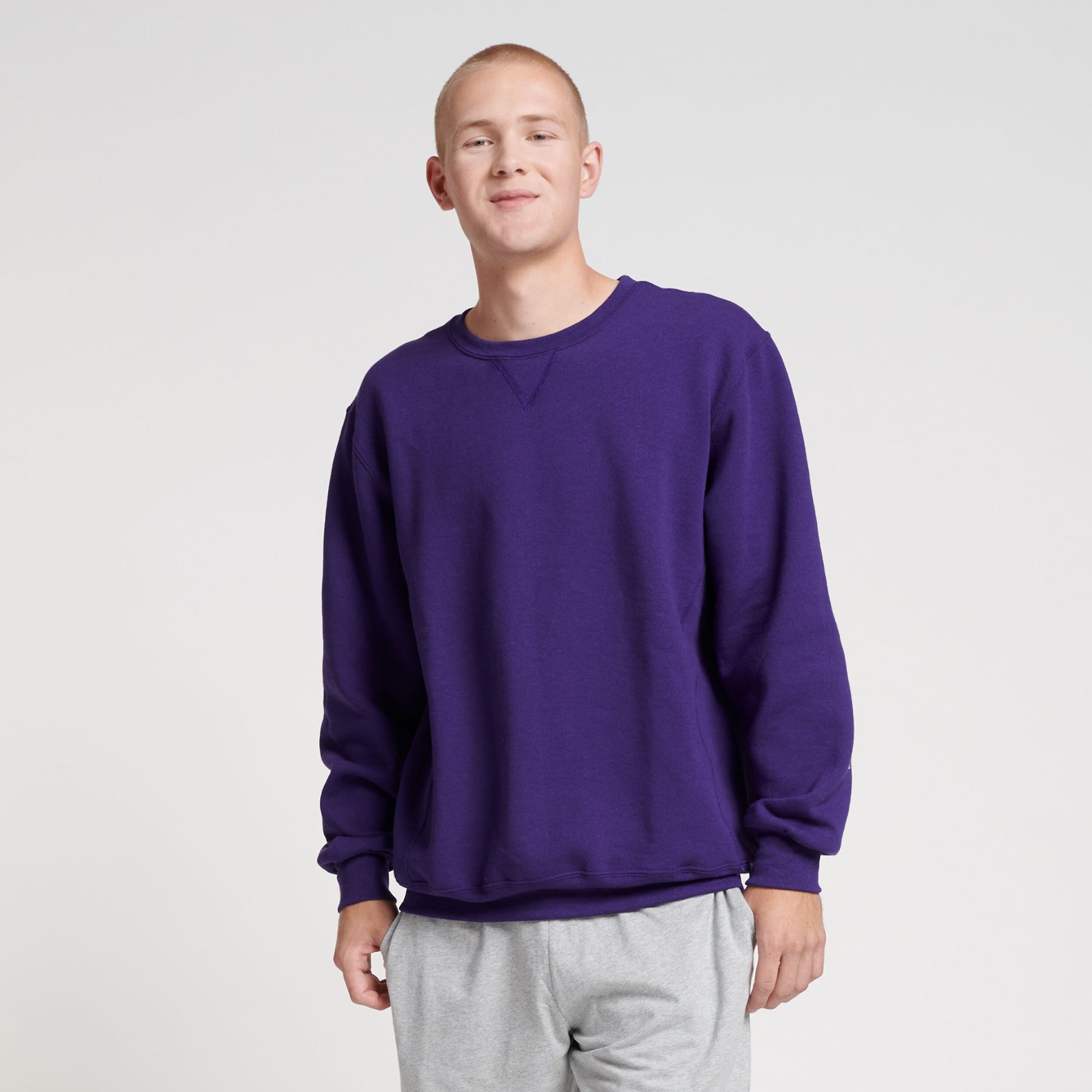 Young man wearing a purple Russell Athletic DRI-POWER Adult Fleece Crew sweatshirt paired with grey sweatpants.