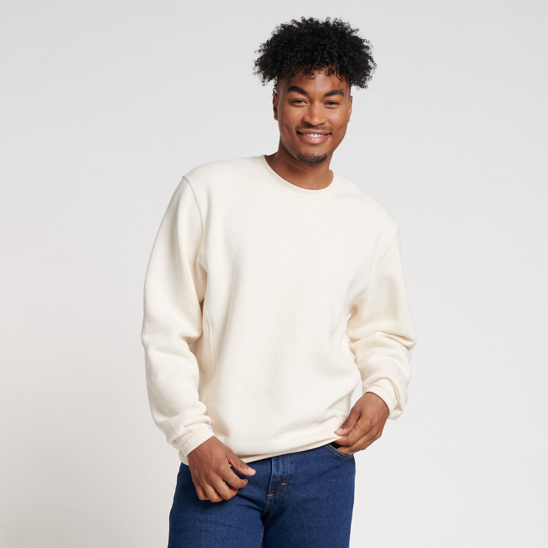 A smiling man wearing a Russell Athletic DRI-POWER® Adult Fleece Crew sweatshirt in vintage white with blue jeans.
