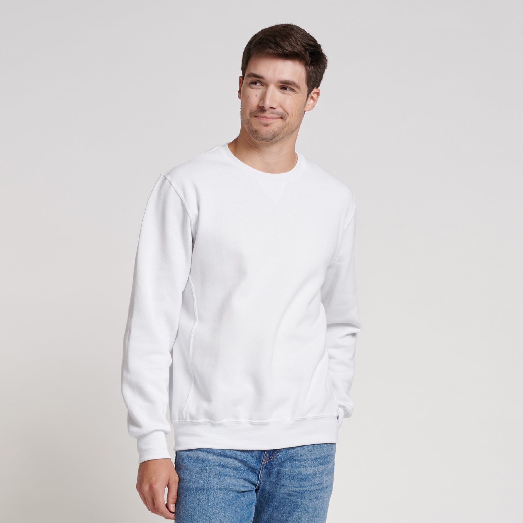 A man wearing a white Russell Athletic DRI-POWER Adult Fleece Crew sweatshirt with blue jeans.