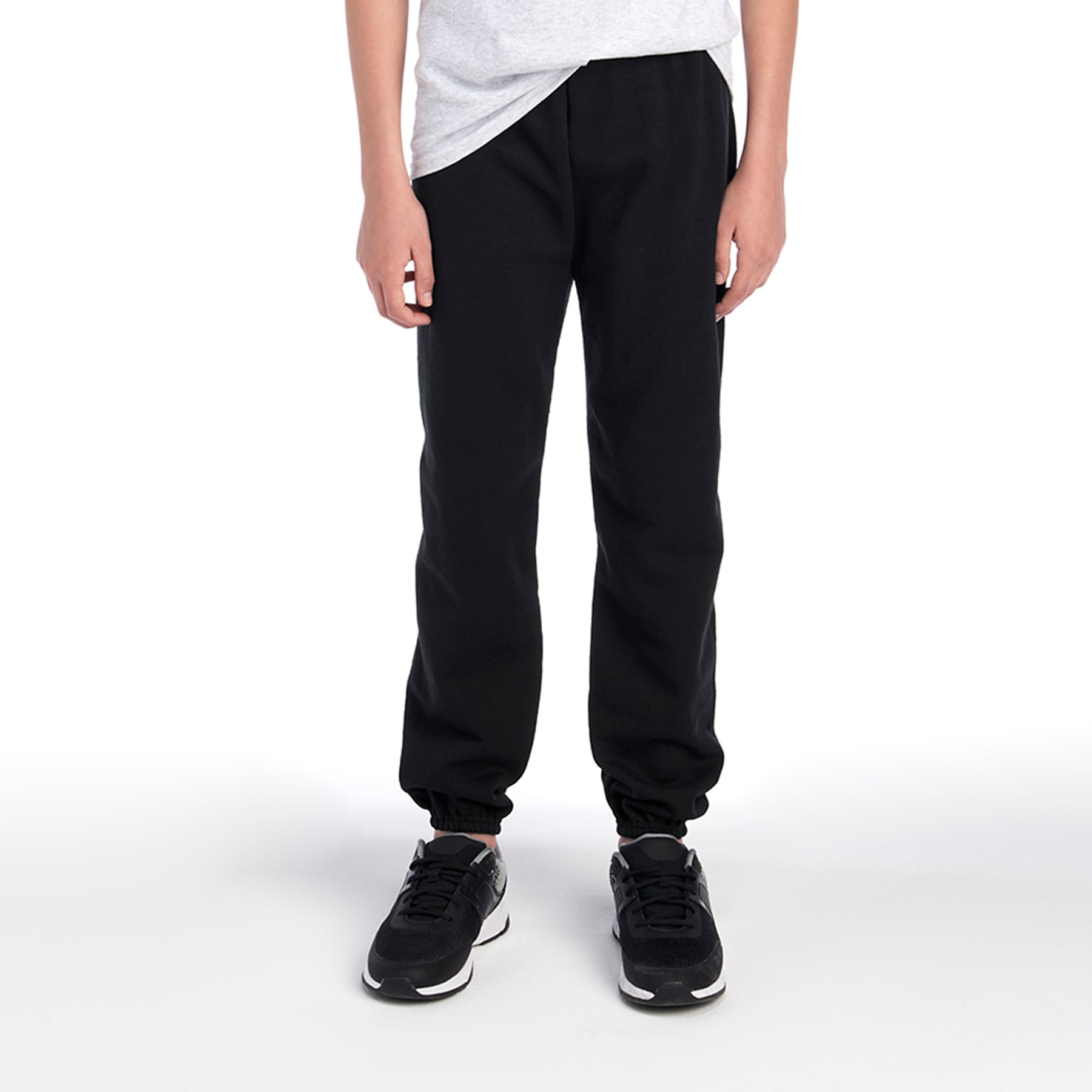 A person wearing Jerzees NuBlend Youth black sweatpants with a grey t-shirt and black sneakers.