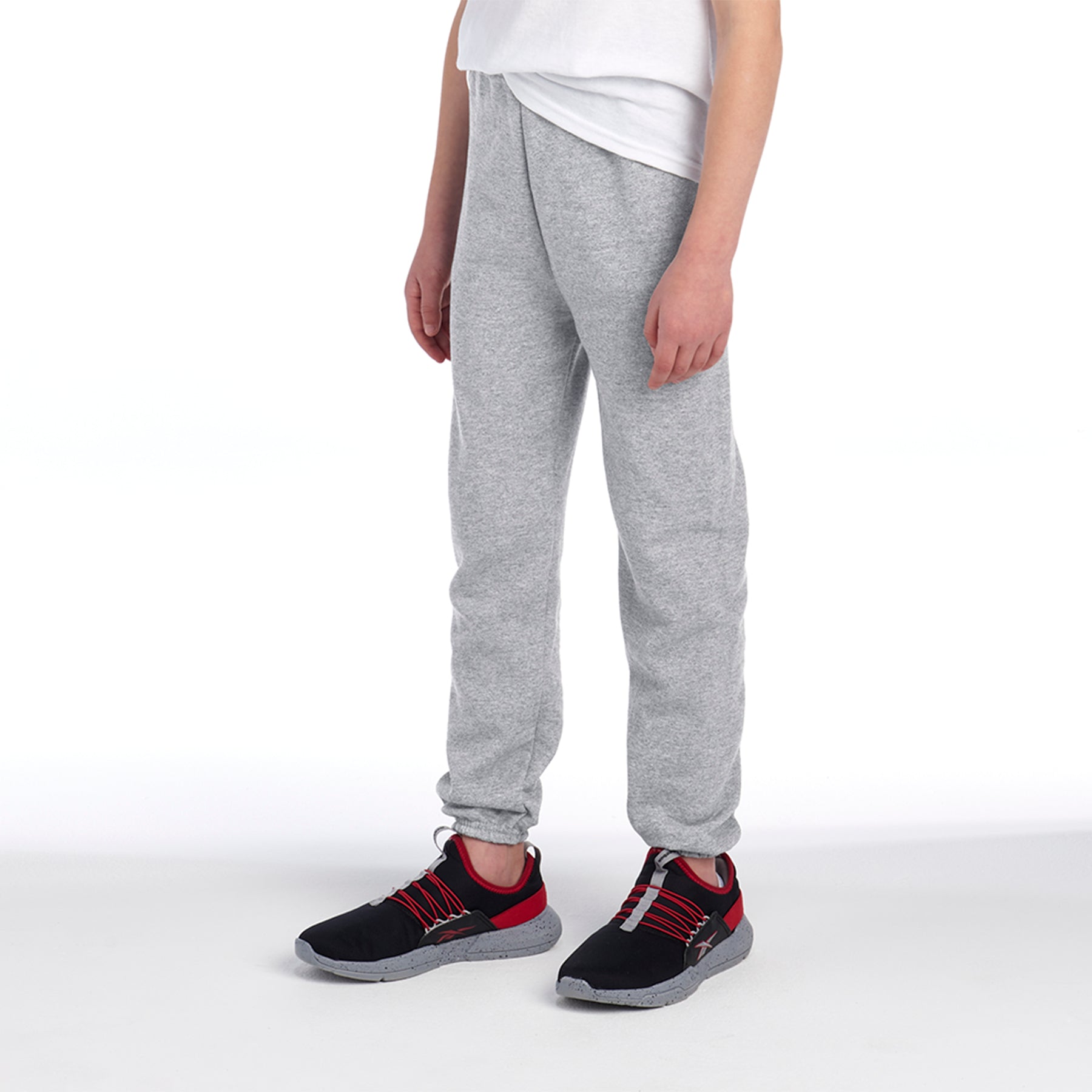 A youth model wearing Jerzees NuBlend® Sweatpants in Oxford grey paired with black and red athletic sneakers.
