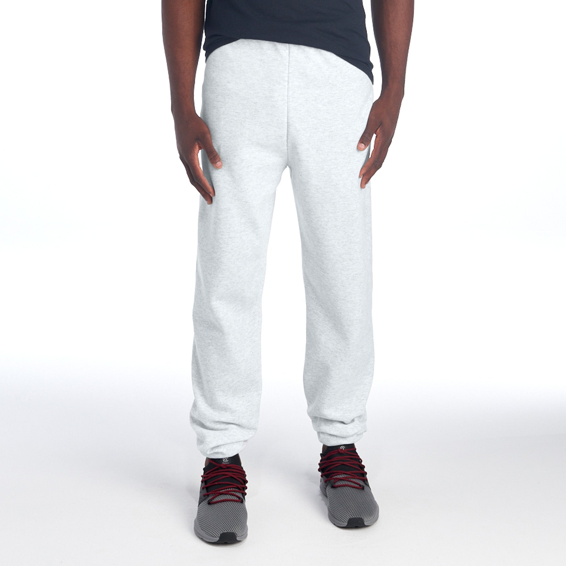 A model wearing ash Jerzees NuBlend® Adult Sweatpants with grey and red sneakers against a white background.