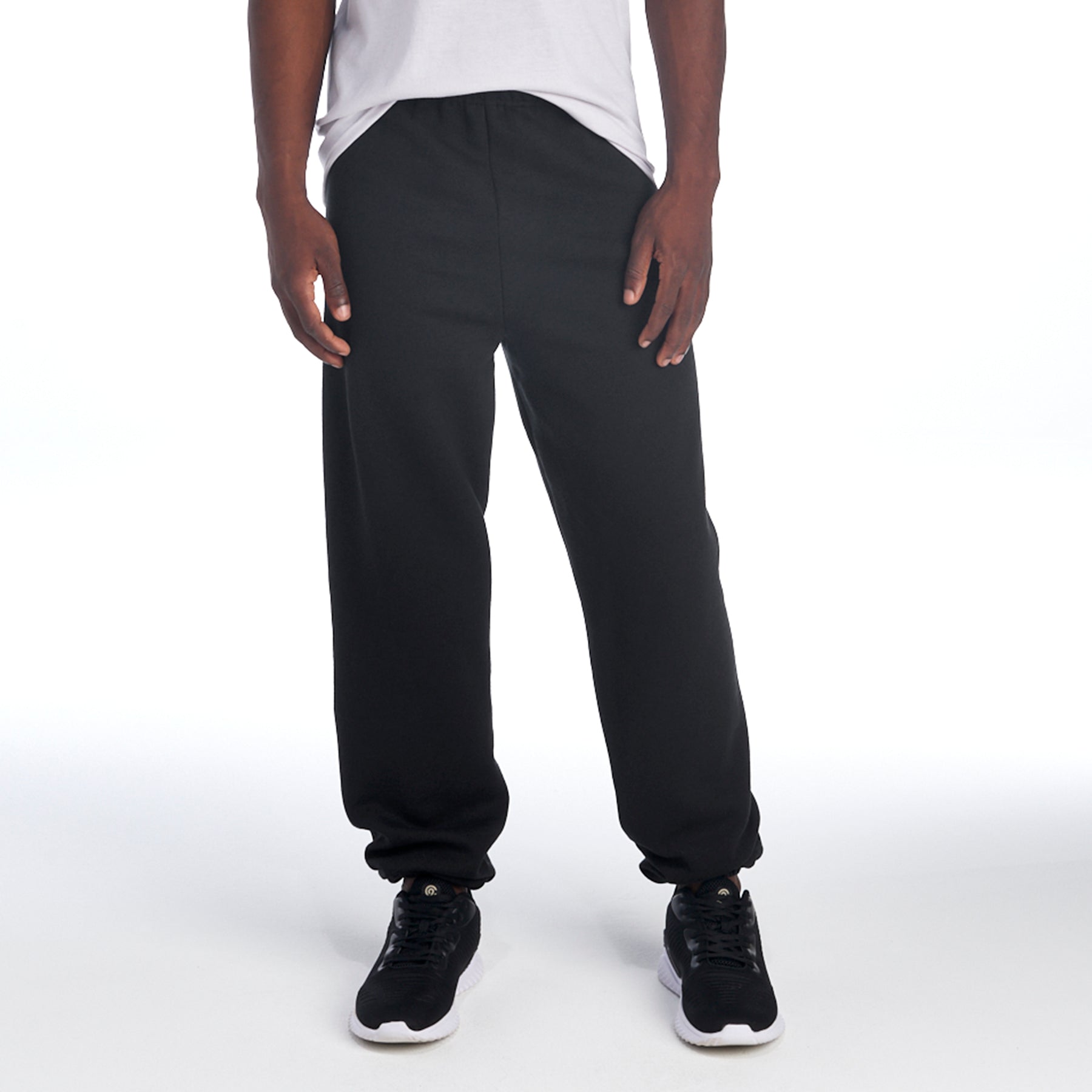 A person wearing black Jerzees NuBlend® Adult Sweatpants with a white t-shirt and athletic shoes.