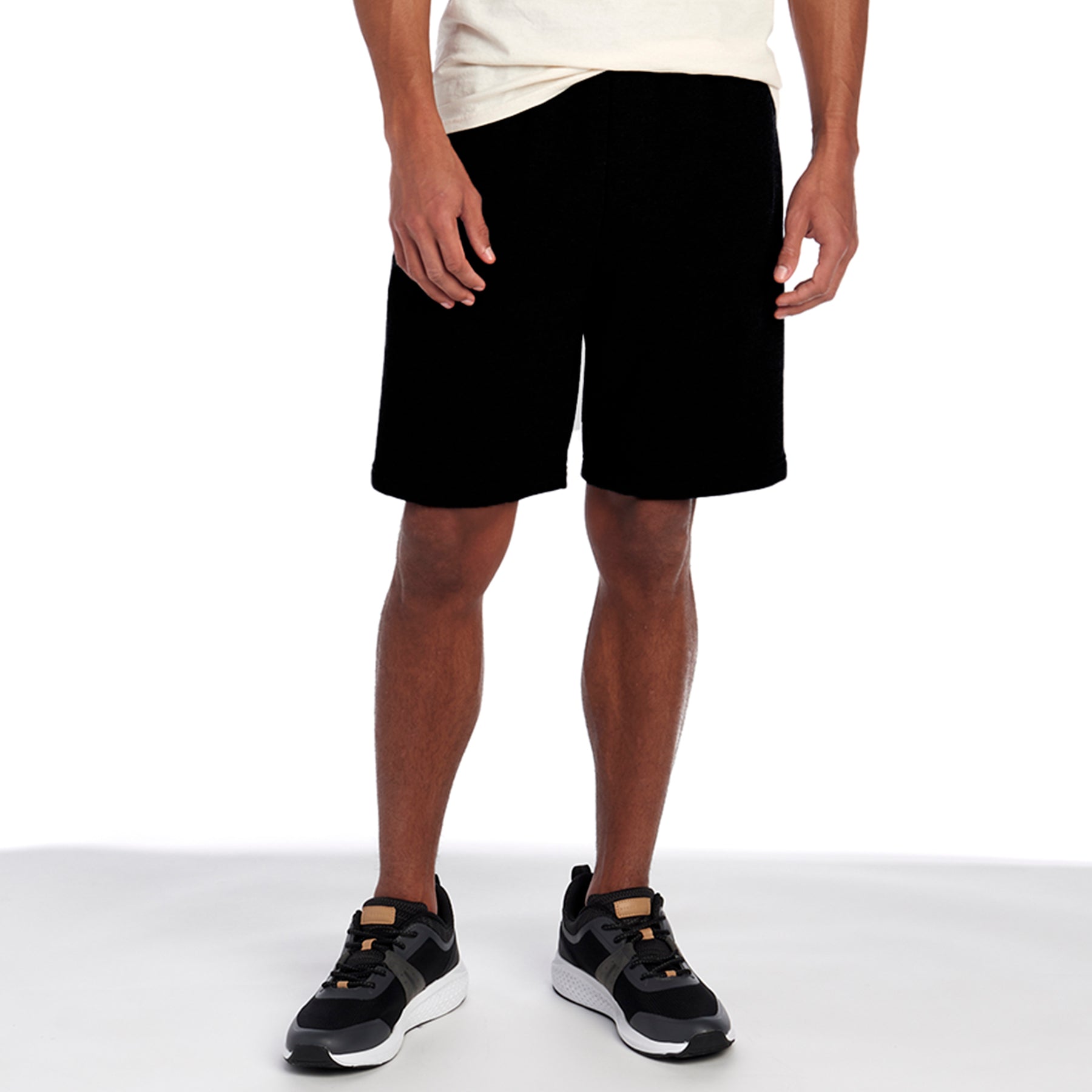 A person wearing black Jerzees NuBlend® Pocketed Sweat Shorts with black athletic sneakers against a white background.