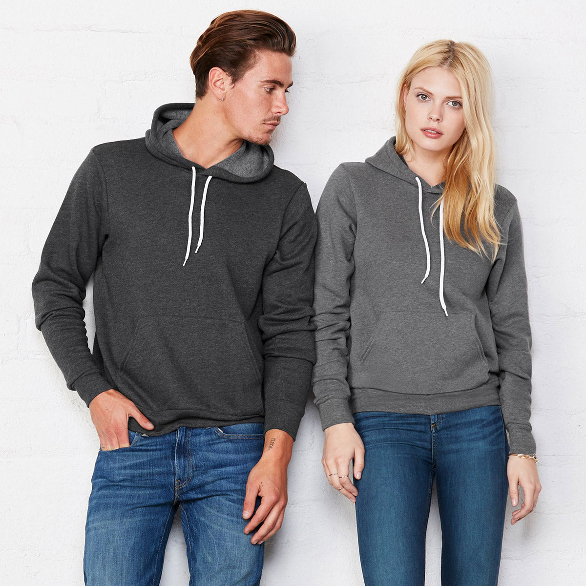 Man and woman modeling Bella+Canvas Unisex Poly-Cotton Fleece Pullover Hoodies in Dark Grey and Deep Heather.