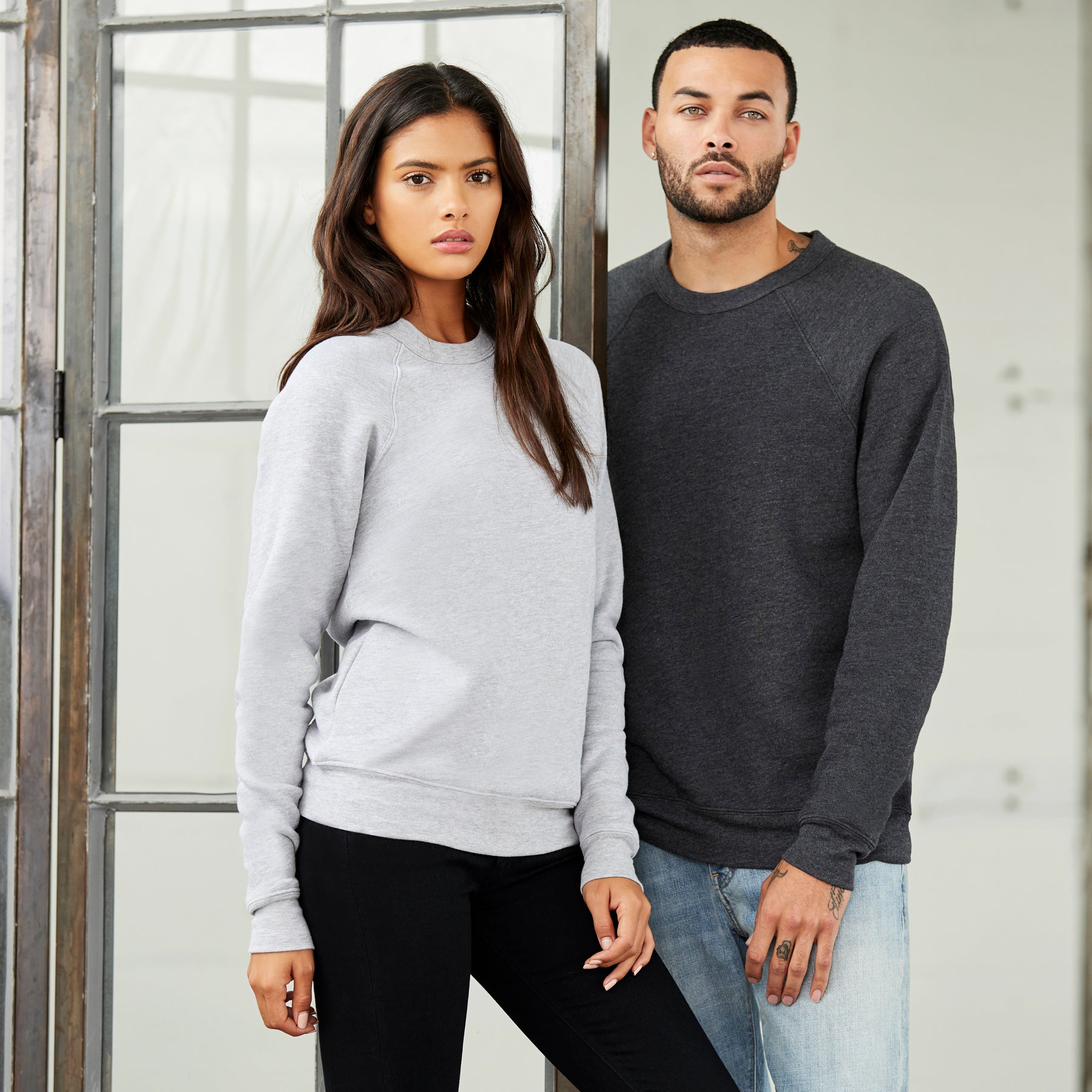 A man and woman modeling a Bella+Canvas Unisex Poly-Cotton Fleece Raglan Sweatshirt in Athletic Heather.