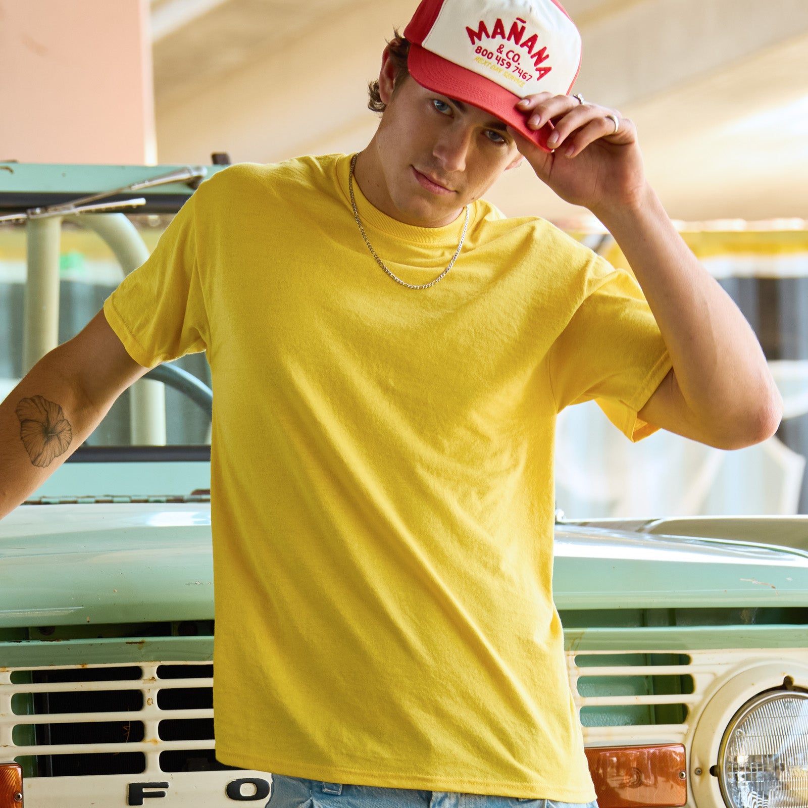 Man posing in a Jerzees Dri-Power Island Yellow unisex T-shirt leaning against a vintage teal vehicle.