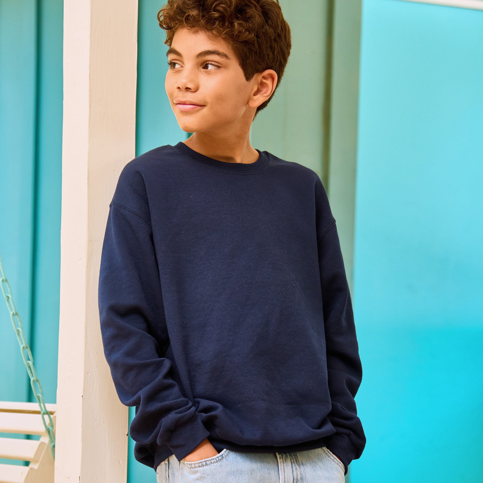 A boy with curly hair wearing a J. Navy Jerzees NuBlend® Youth Sweatshirt with hands in his pockets.