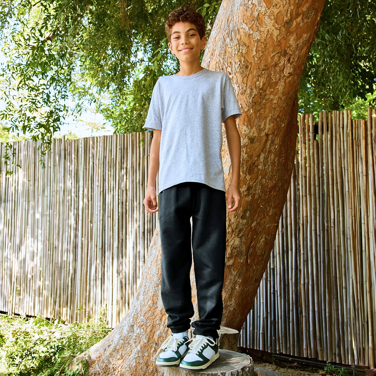 A young boy wearing Jerzees NuBlend® Youth Sweatpants in black, paired with a gray t-shirt, standing outdoors.
