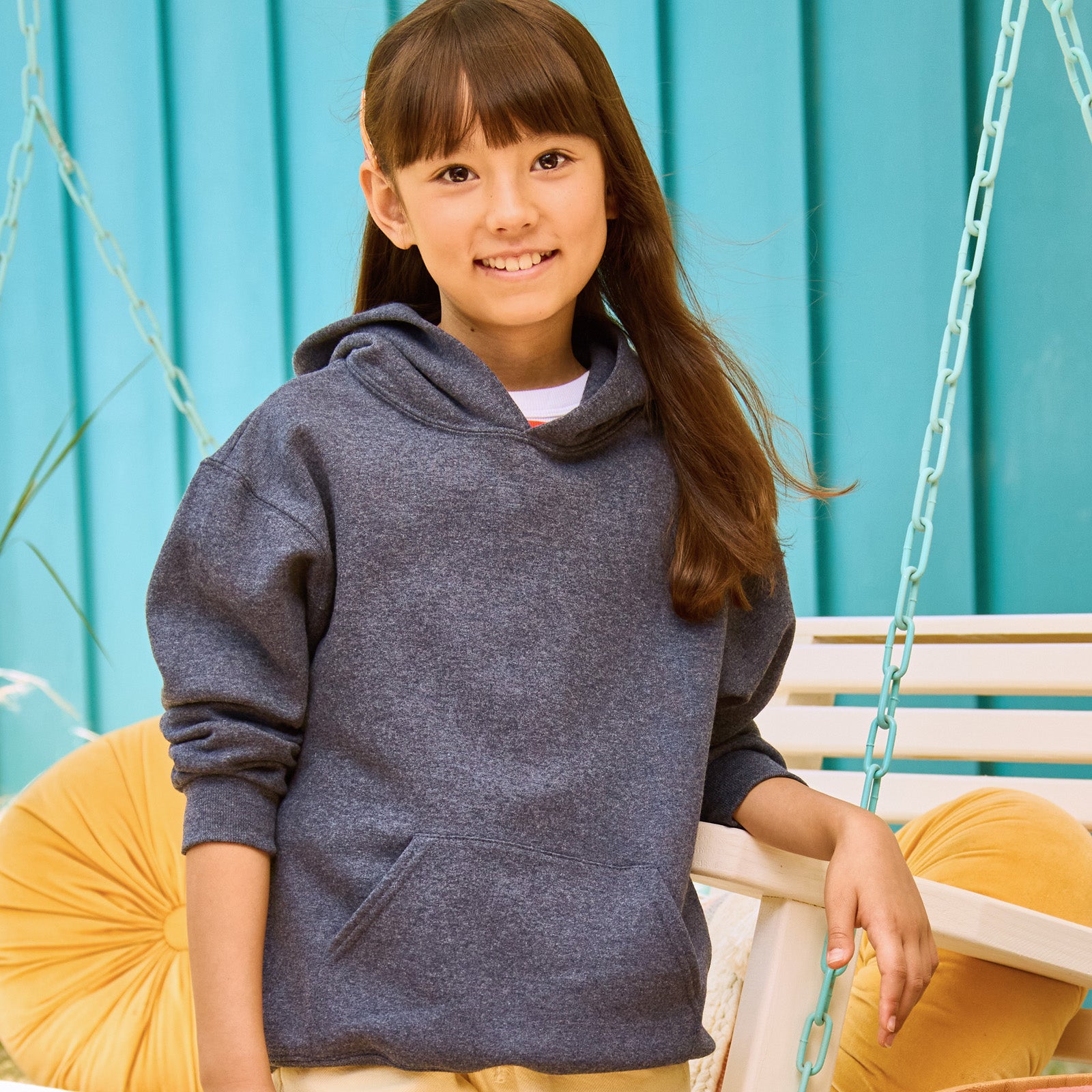 A young girl smiling while wearing a Jerzees NuBlend Youth Hooded Sweatshirt in Black Heather.