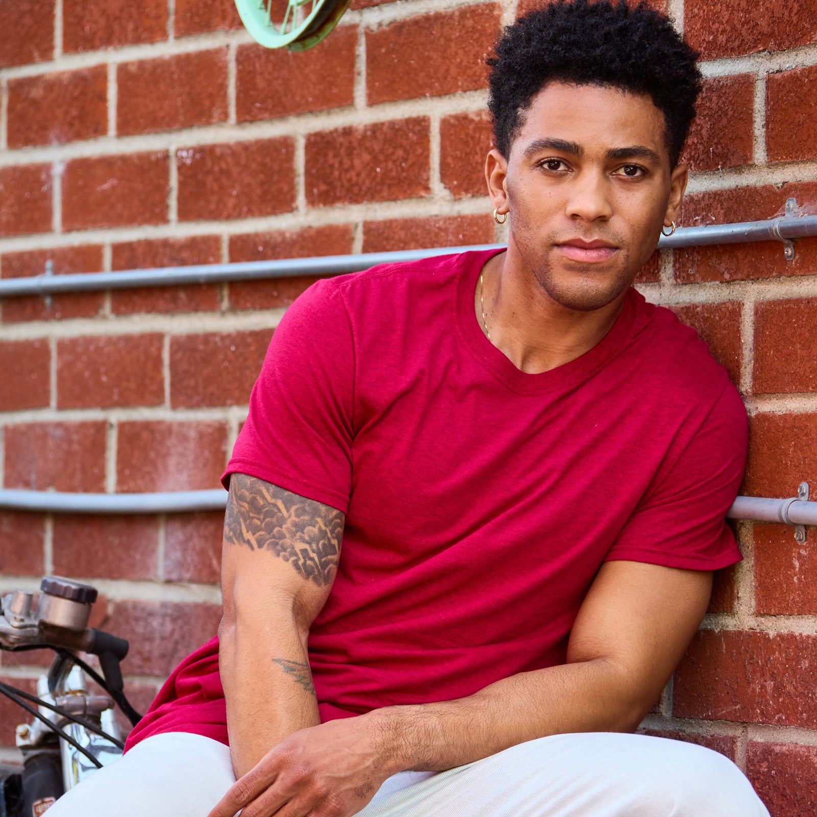 A man wearing a Peppered Red Heather Jerzees Ultimate® Ring-Spun Unisex T-Shirt against a brick wall.