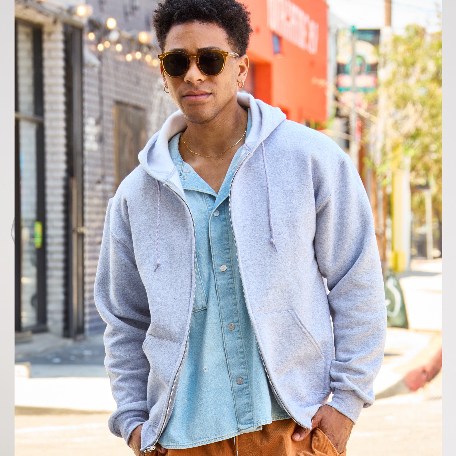 Young man wearing a Jerzees Rugged Unisex Full-Zip Hooded Sweatshirt in Athletic Heather over a light blue denim shirt.