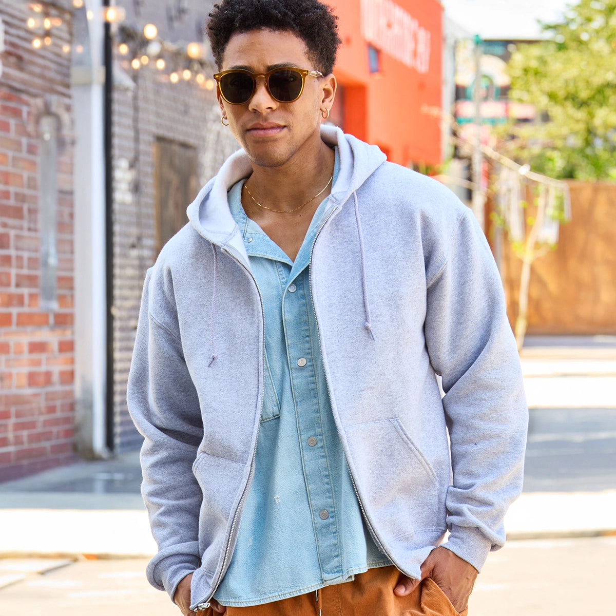 Young man wearing a Jerzees Rugged Unisex Full-Zip Hooded Sweatshirt in Athletic Heather over a light blue denim shirt.