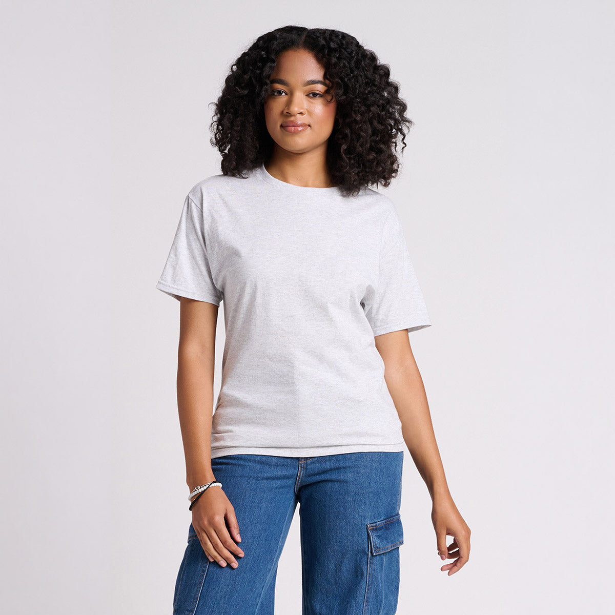 A woman wearing an ash Jerzees Classics unisex t-shirt paired with blue cargo jeans against a light background.