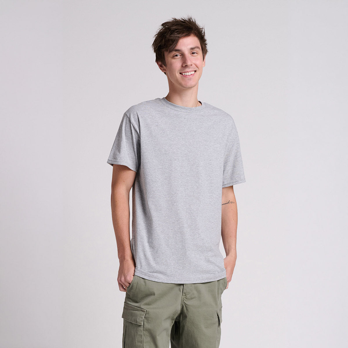 A young man wearing an Athletic Heather Jerzees Classics Unisex T-Shirt with olive green cargo pants.