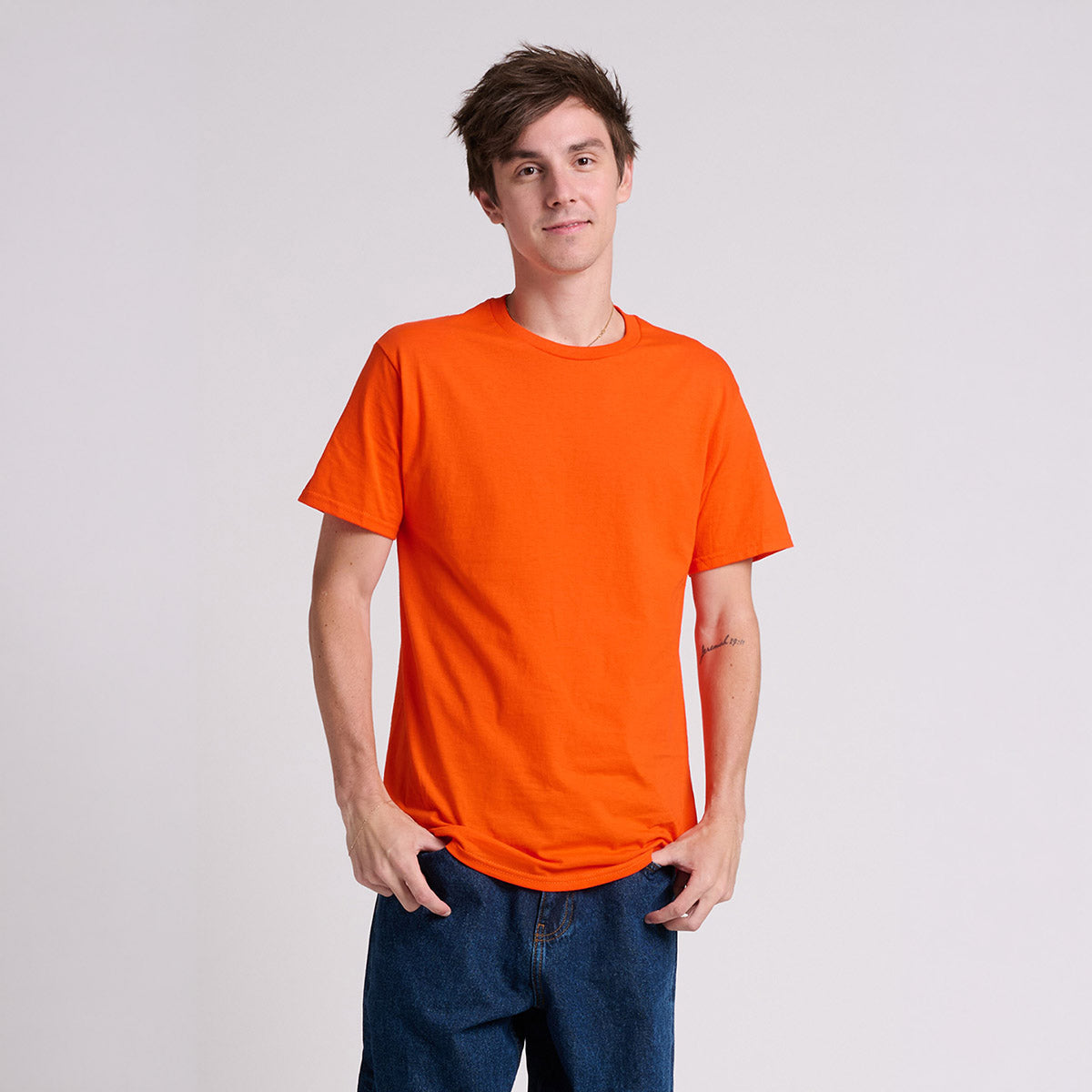 A man wearing a Jerzees Classics unisex t-shirt in burnt orange paired with blue jeans.