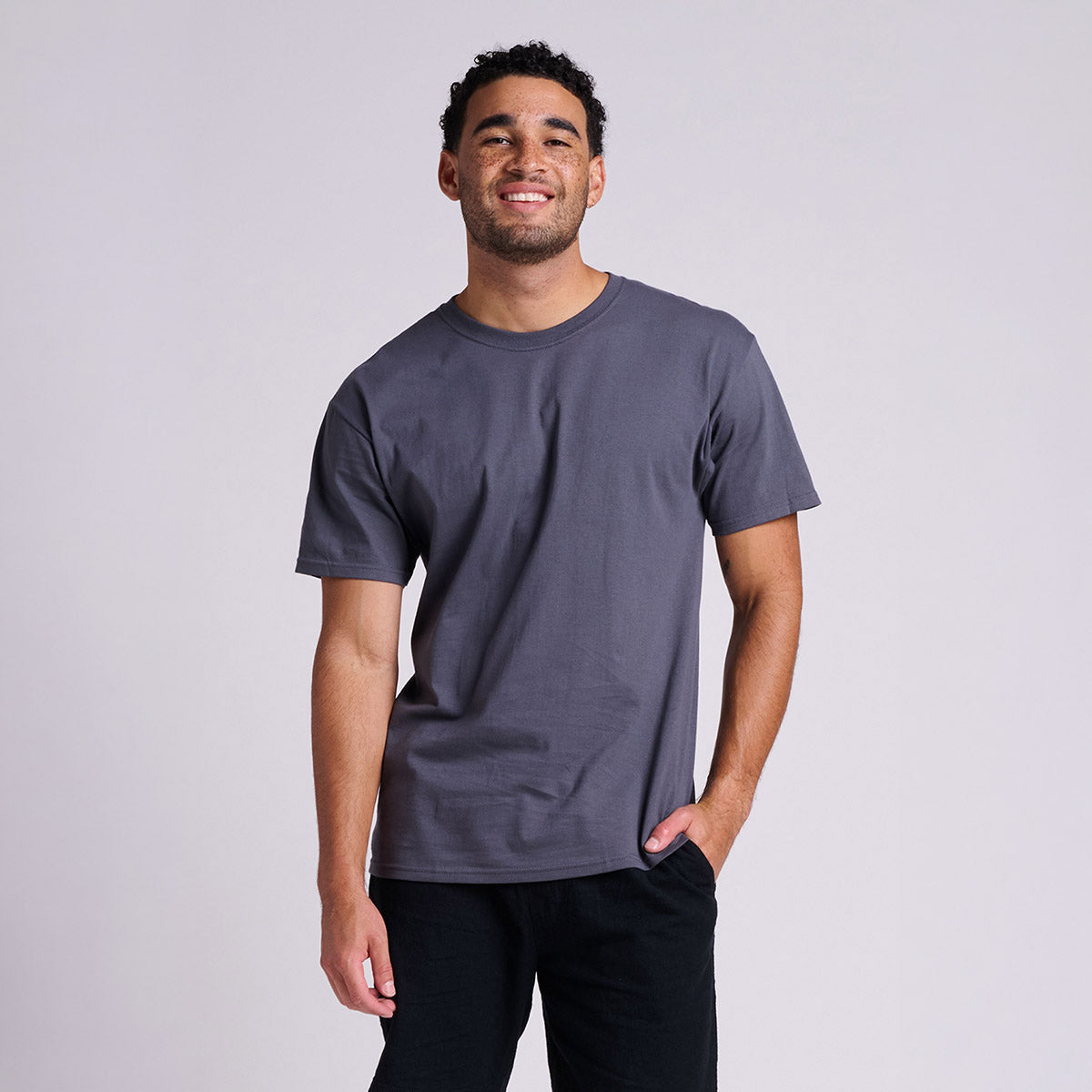 A young man wearing a charcoal grey Jerzees Classics Unisex T-Shirt against a plain light background.