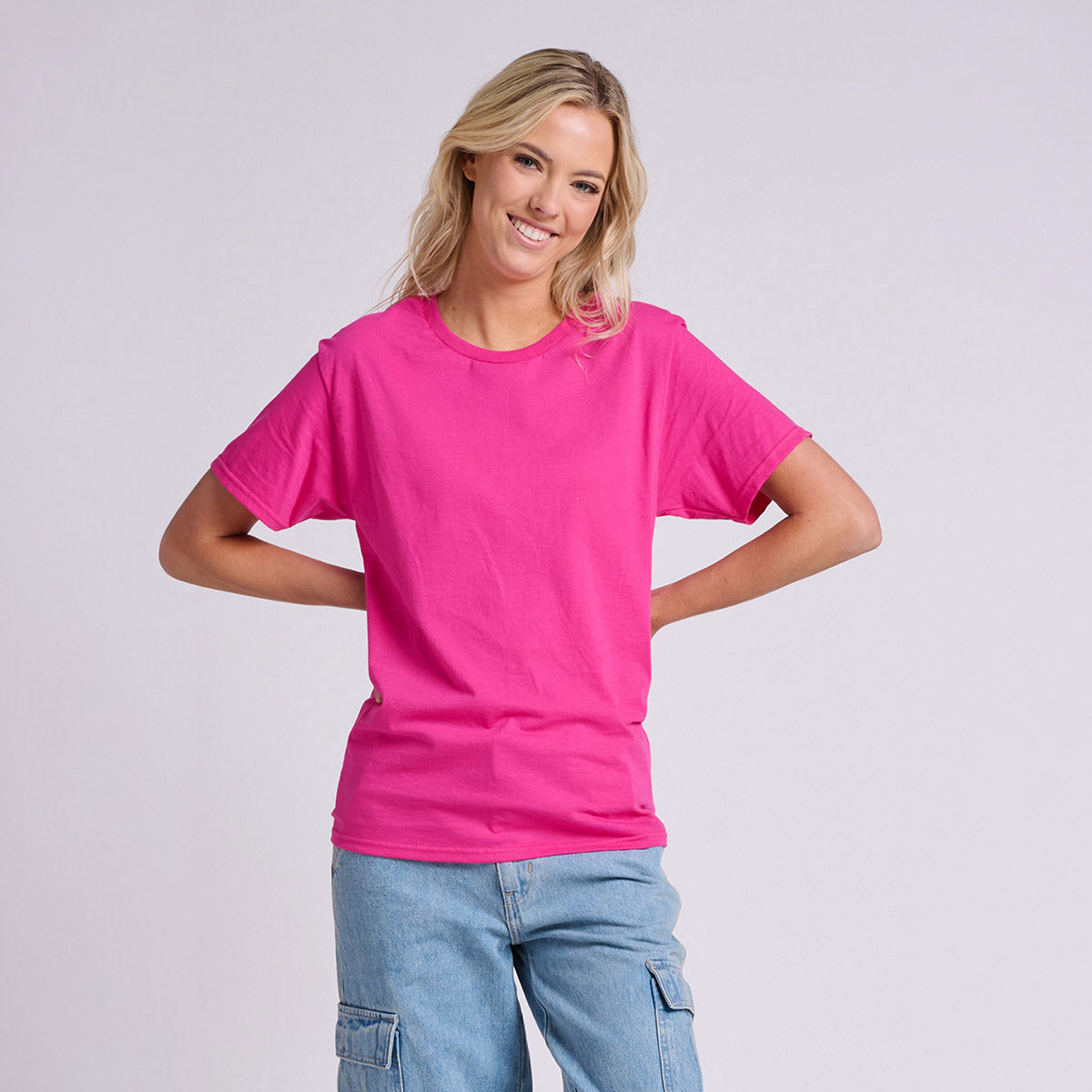 Smiling woman wearing a Cyber Pink Jerzees Classics Unisex T-Shirt with her hands on her hips.