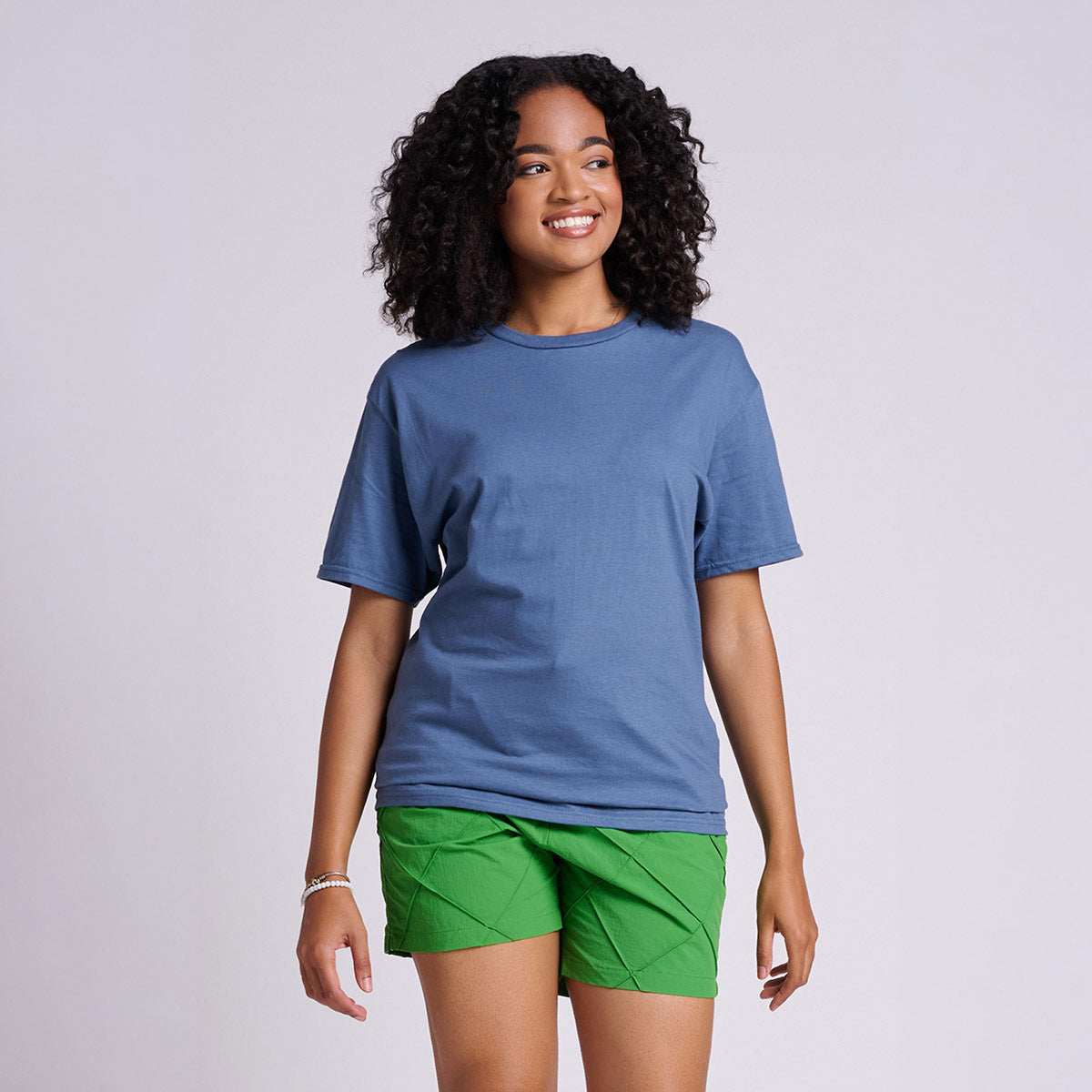 A woman with curly hair wears a Denim Jerzees Classics Unisex T-Shirt with bright green shorts.