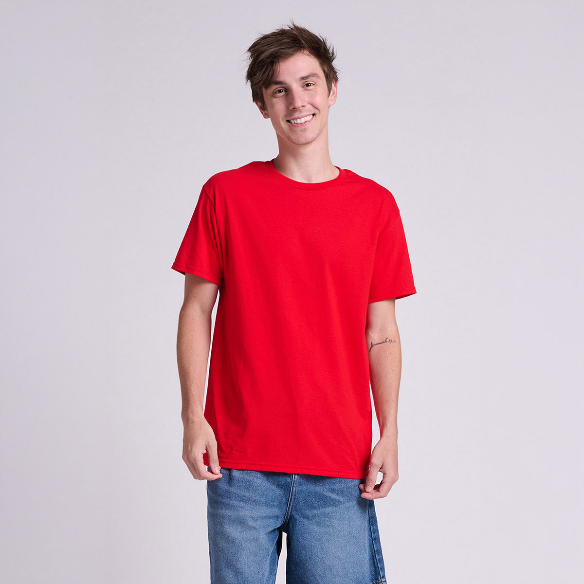 A young man wearing a Fiery Red Jerzees Classics unisex T-shirt against a plain studio background.