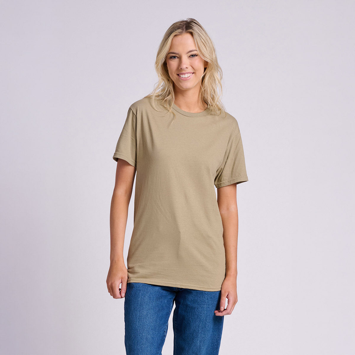Woman smiling while wearing a khaki Jerzees Classics unisex t-shirt with blue jeans.