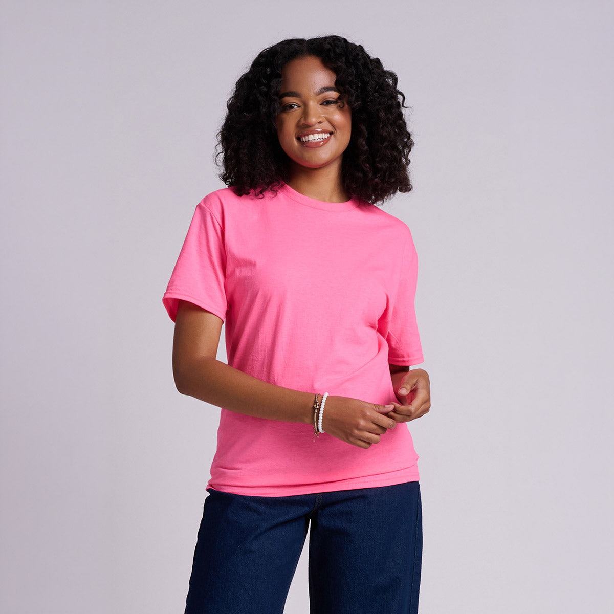 Woman smiling while wearing a neon pink Jerzees Classics Unisex T-Shirt paired with blue jeans.