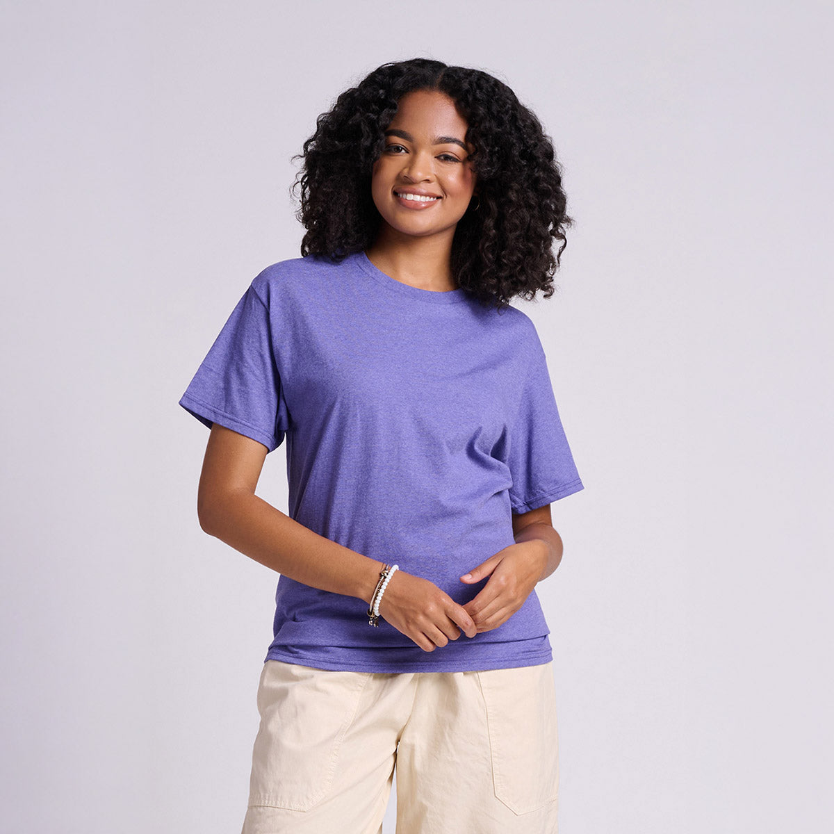 A woman with curly hair wearing a Retro Heather Purple Jerzees Classics Unisex T-Shirt against a light background.