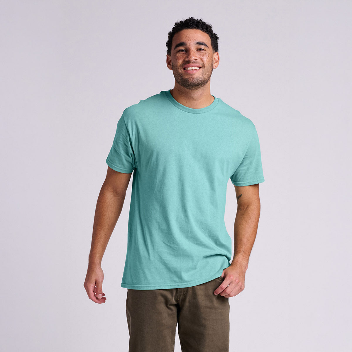 Man smiling while wearing a sage green Jerzees Classics Unisex T-Shirt against a grey background.