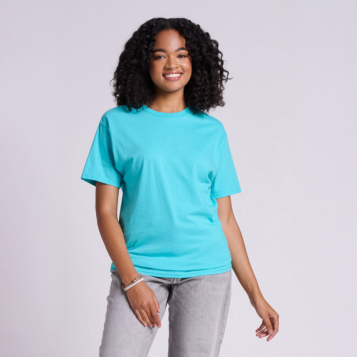 A smiling model wearing a Jerzees Classics unisex t-shirt in scuba blue paired with gray jeans.