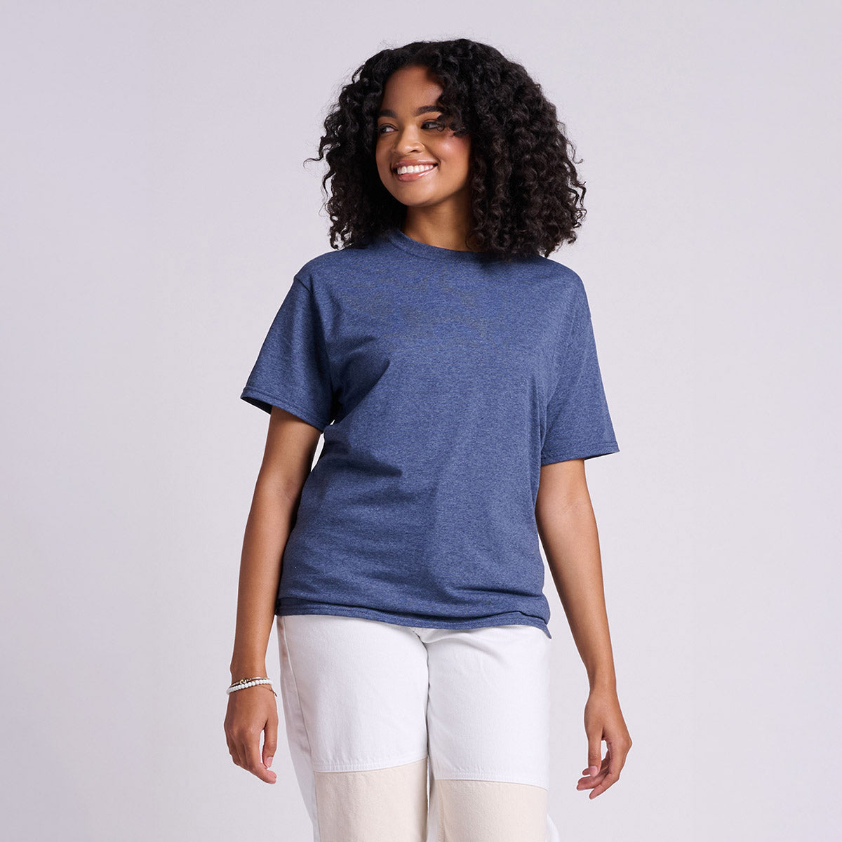 A woman with curly hair wearing a Vintage Heather Navy Jerzees Classics Unisex T-Shirt against a plain background.