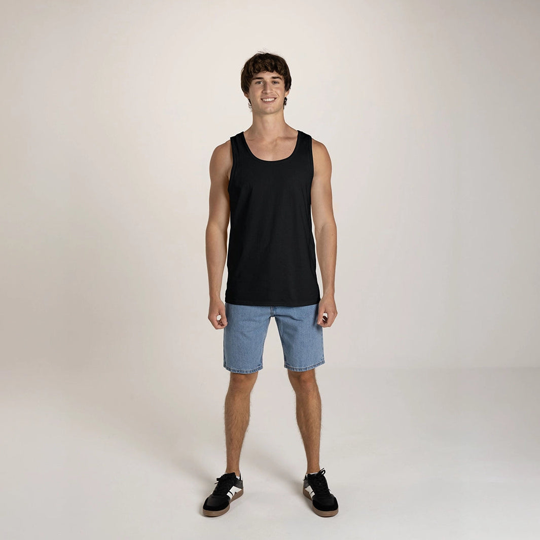 A young man wearing a black JERZEES Classics Unisex Tank top with light blue denim shorts and sneakers.