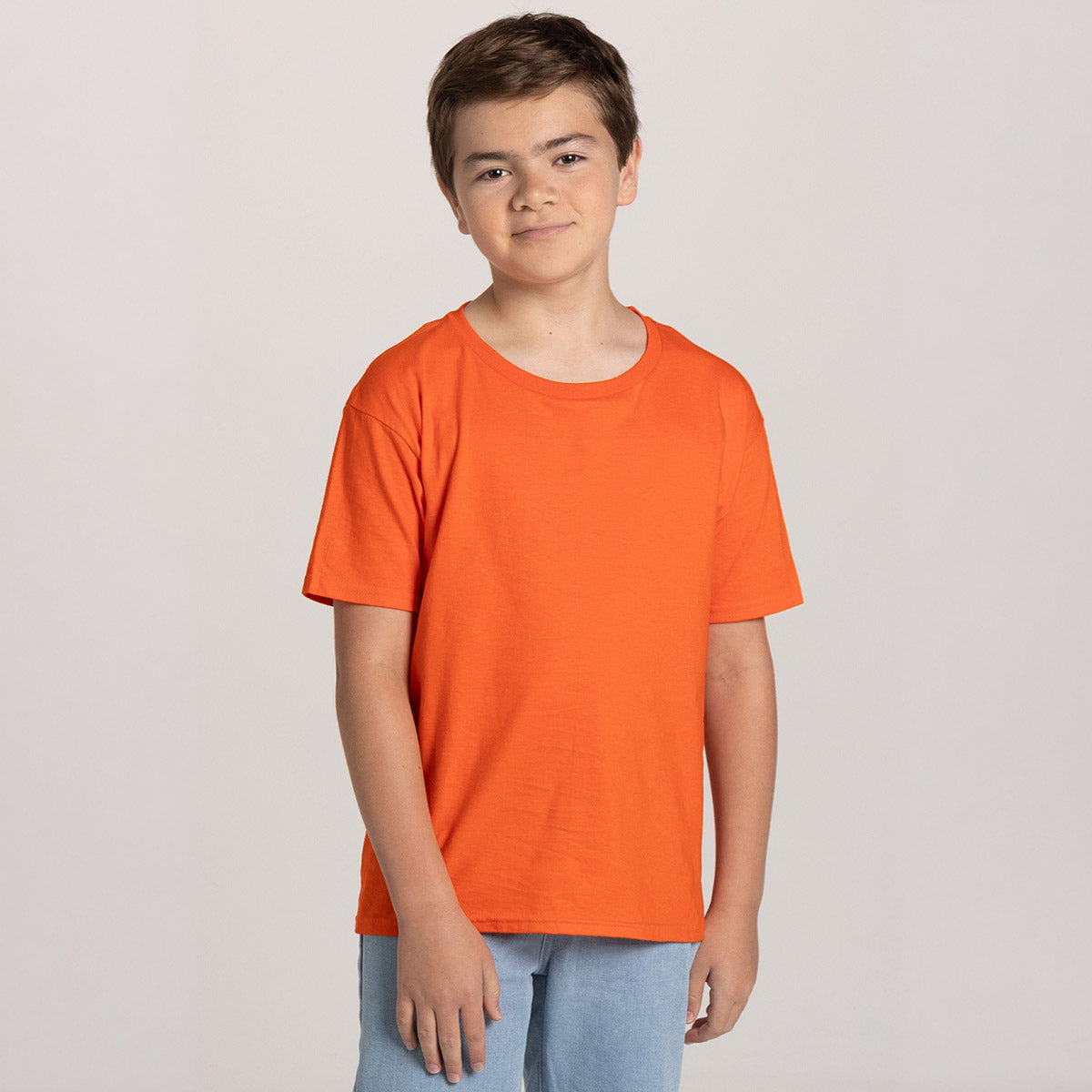 A young boy wearing a burnt orange Jerzees Classics youth t-shirt against a plain grey studio background.