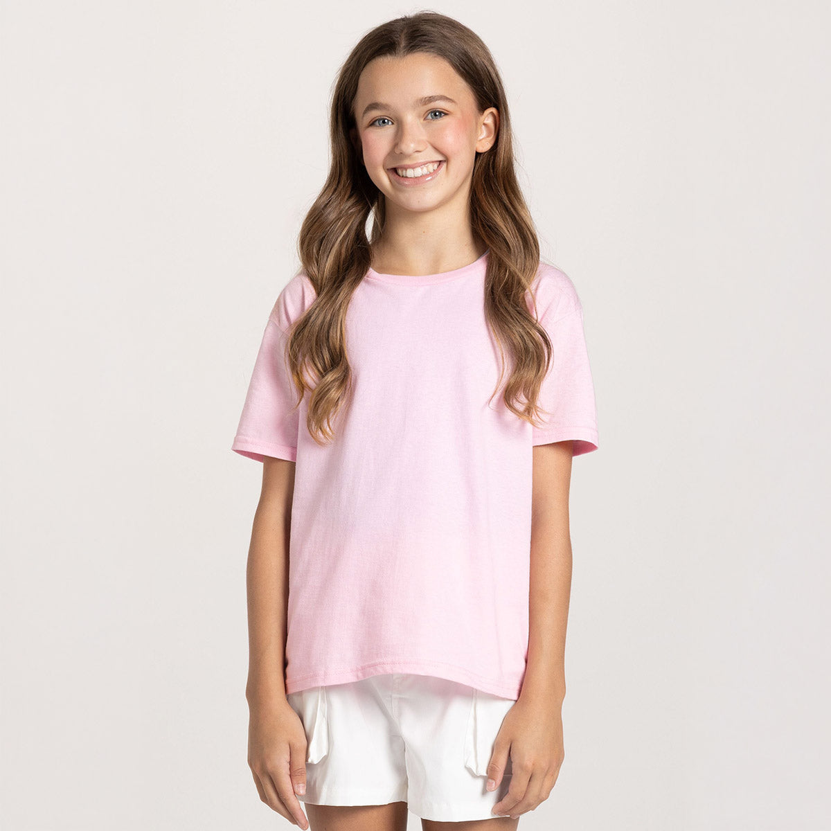 A young girl wearing a Classic Pink Jerzees Classics Youth T-Shirt standing against a white background.