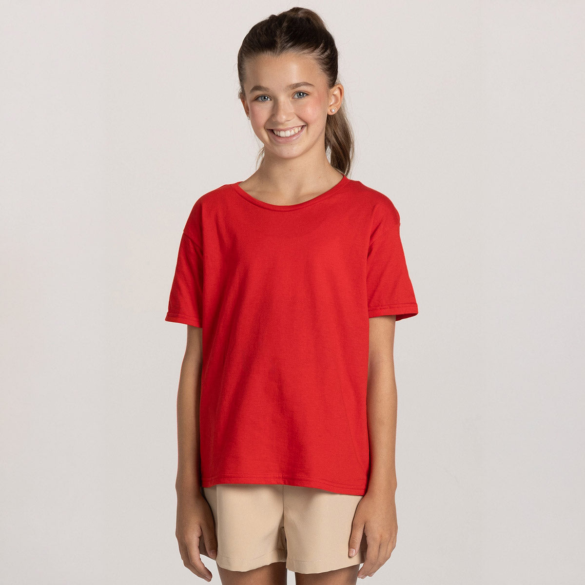 A girl wearing a Jerzees Classics Youth T-Shirt in fiery red paired with beige shorts.