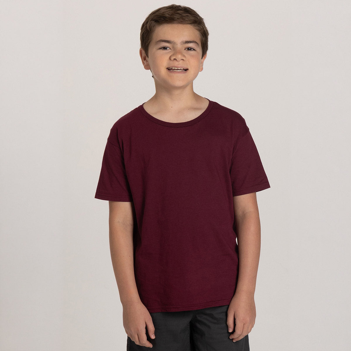 A boy wearing a maroon Jerzees Classics Youth T-Shirt against a plain light gray background.